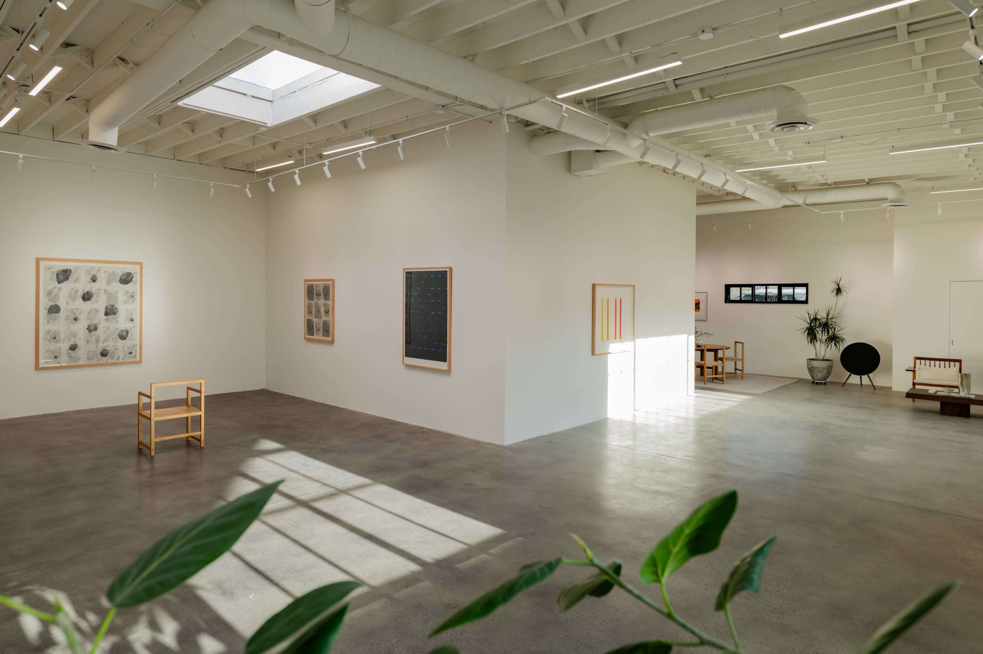 The image depicts a modern art gallery with minimalist decor, featuring several framed artworks on the walls and various seating arrangements.