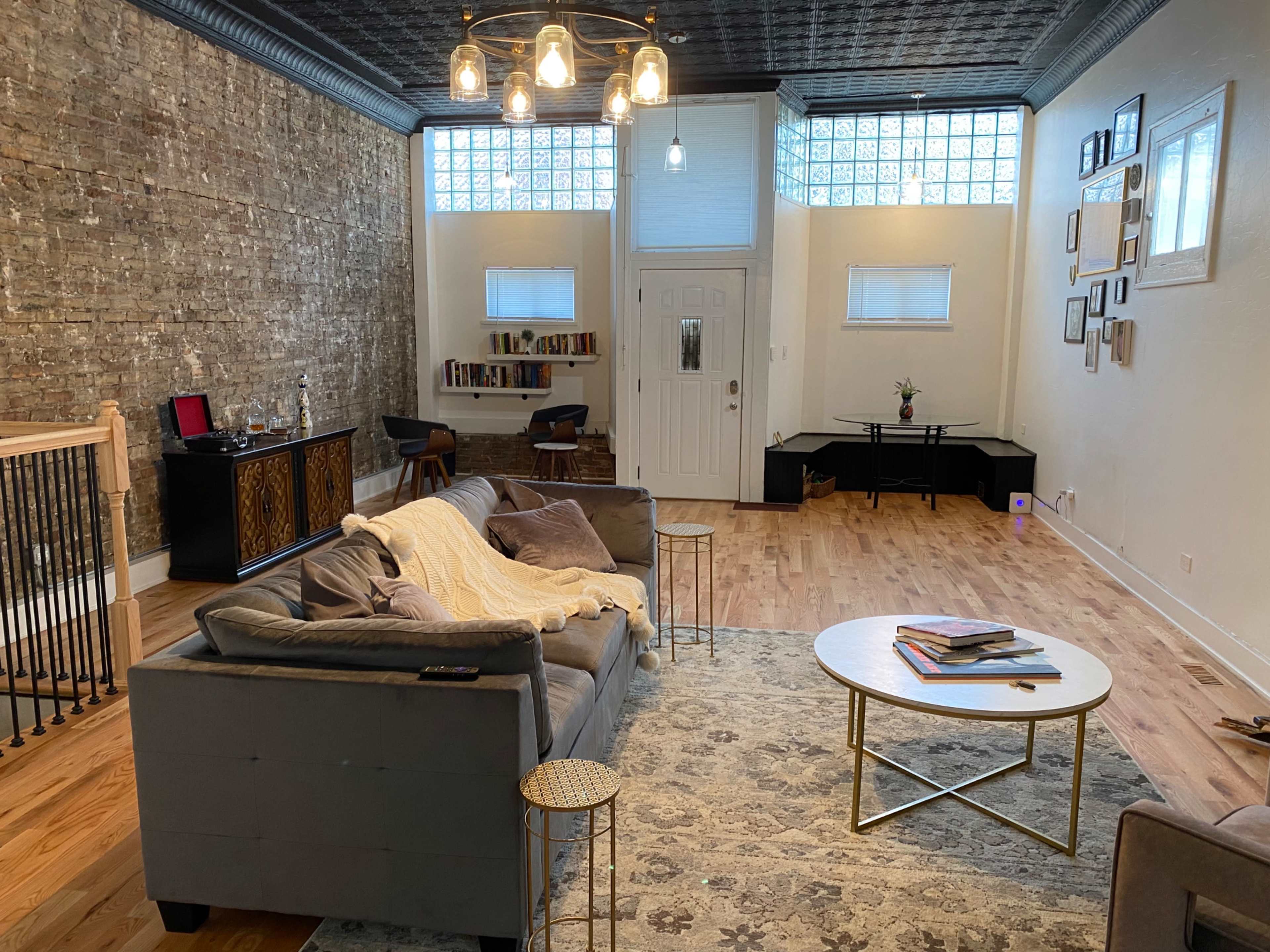 A spacious living room with a brick wall, hardwood flooring, and a sofa facing a round coffee table, illuminated by pendant lights above.