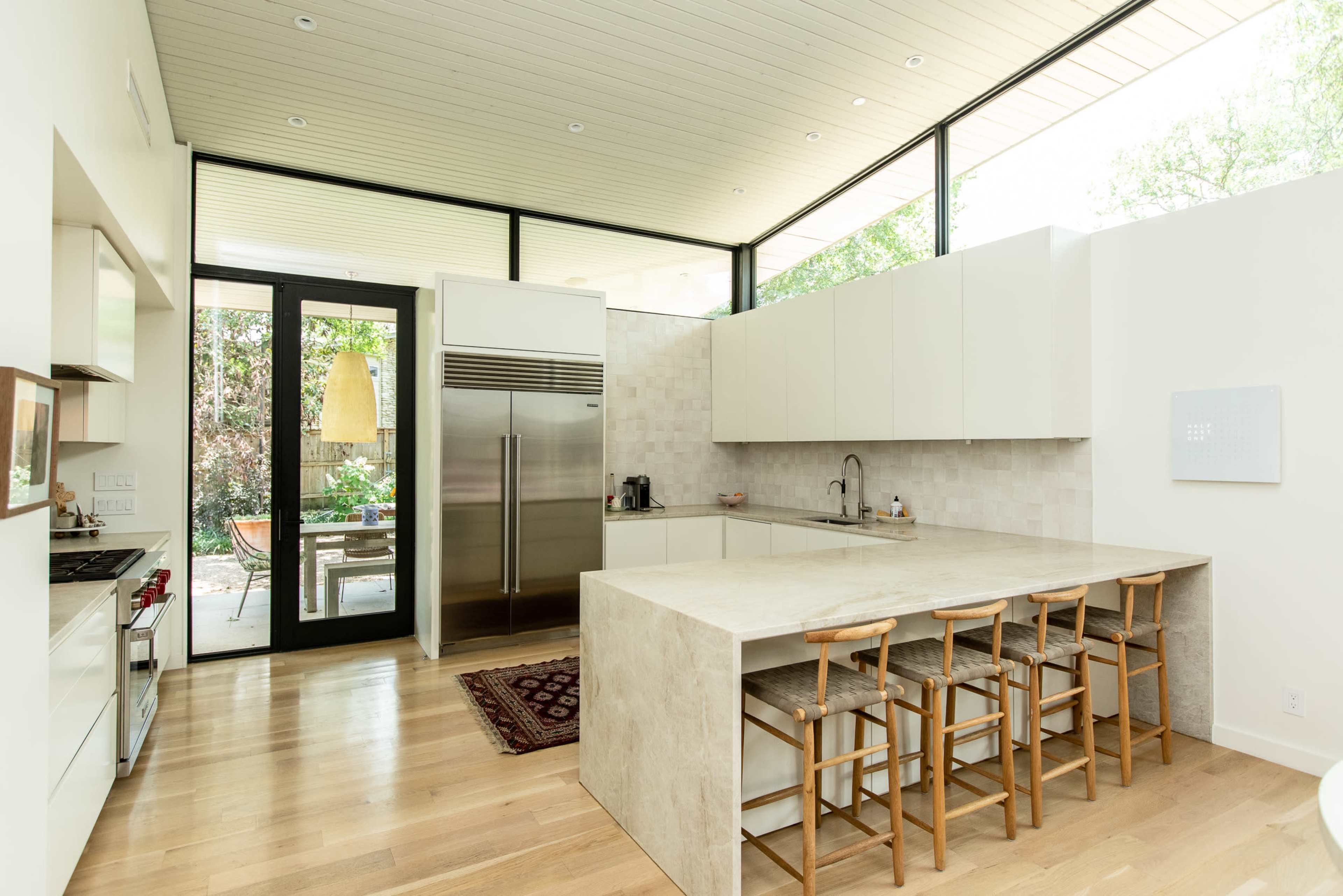 A modern kitchen with a large island, sleek cabinetry, and large windows that provide views of an outdoor garden.