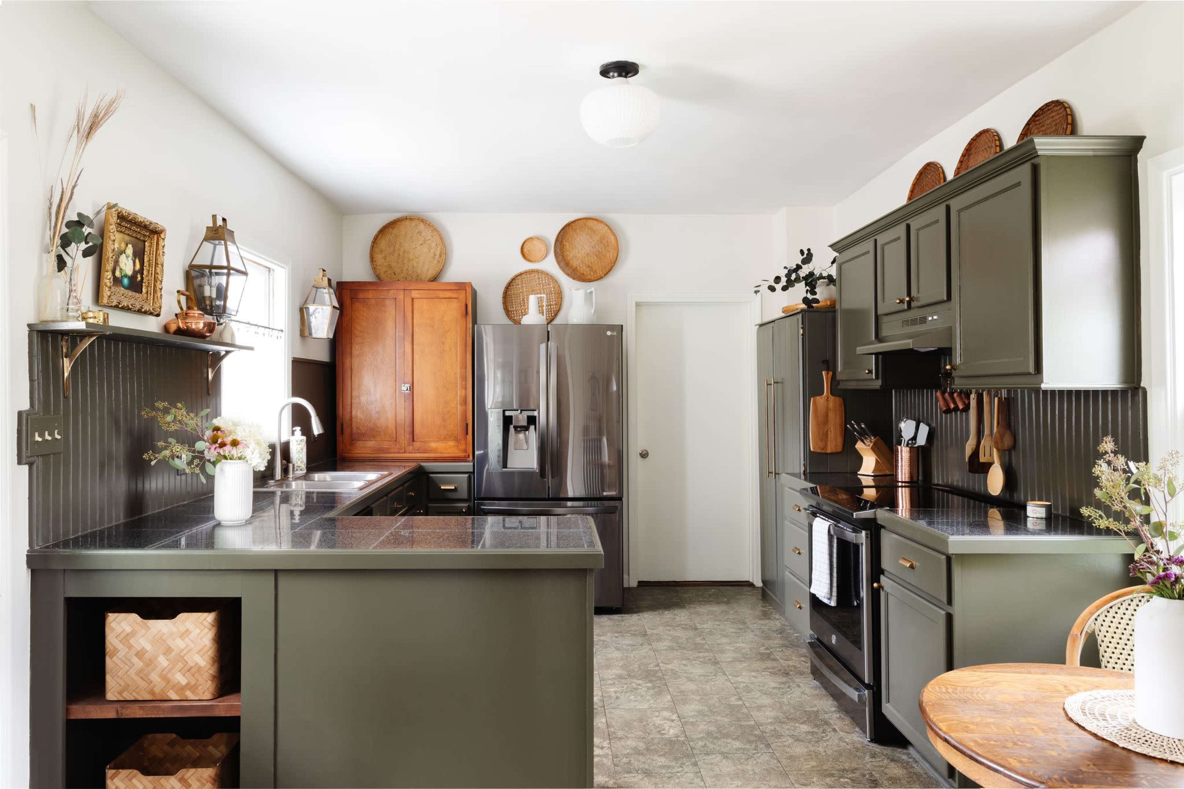 A modern kitchen featuring dark green cabinetry, stainless steel appliances, and a round dining table with woven decor elements.