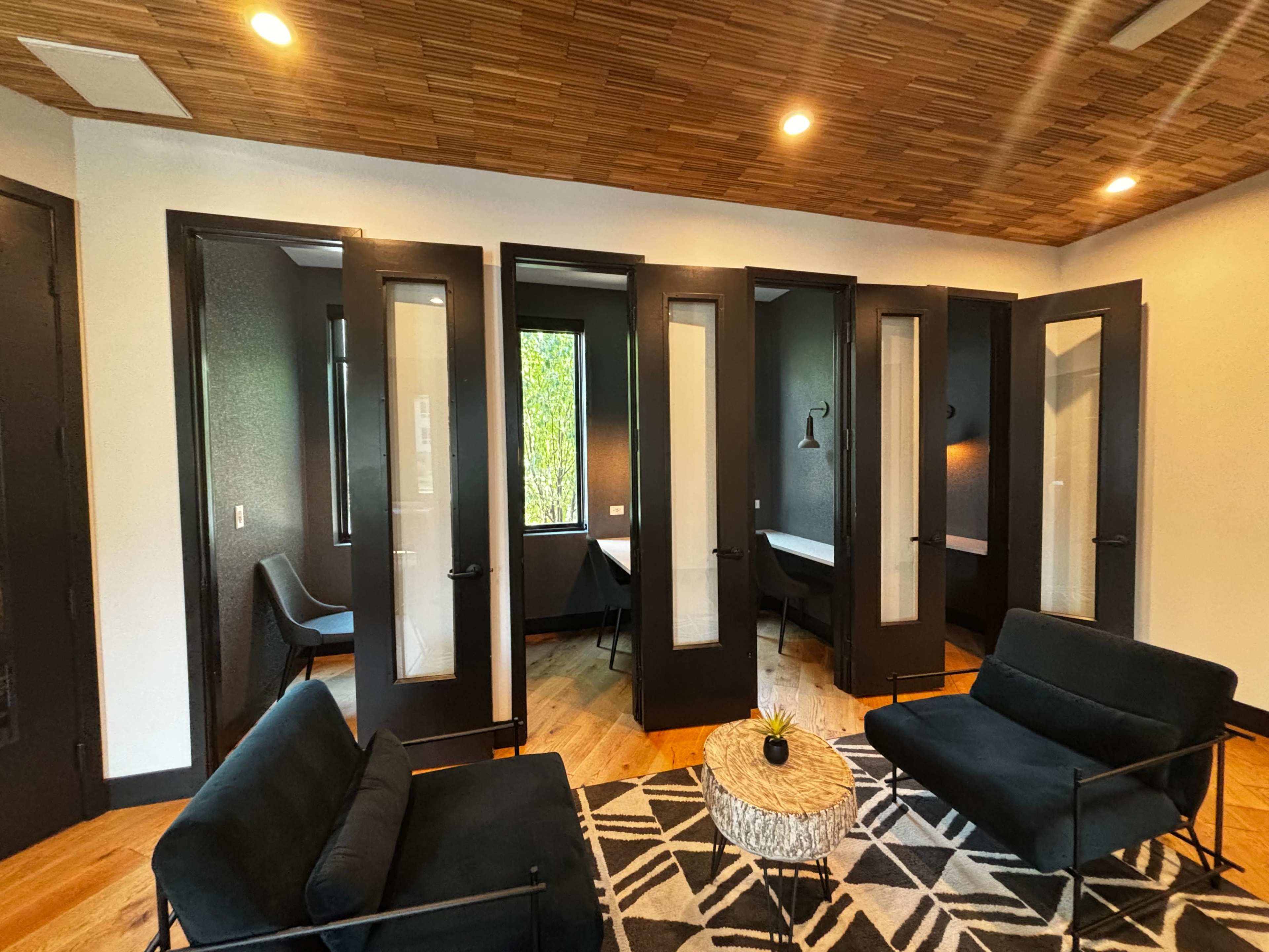 A modern room with dark doors and large windows, featuring two black sofas and a round coffee table on a patterned rug.