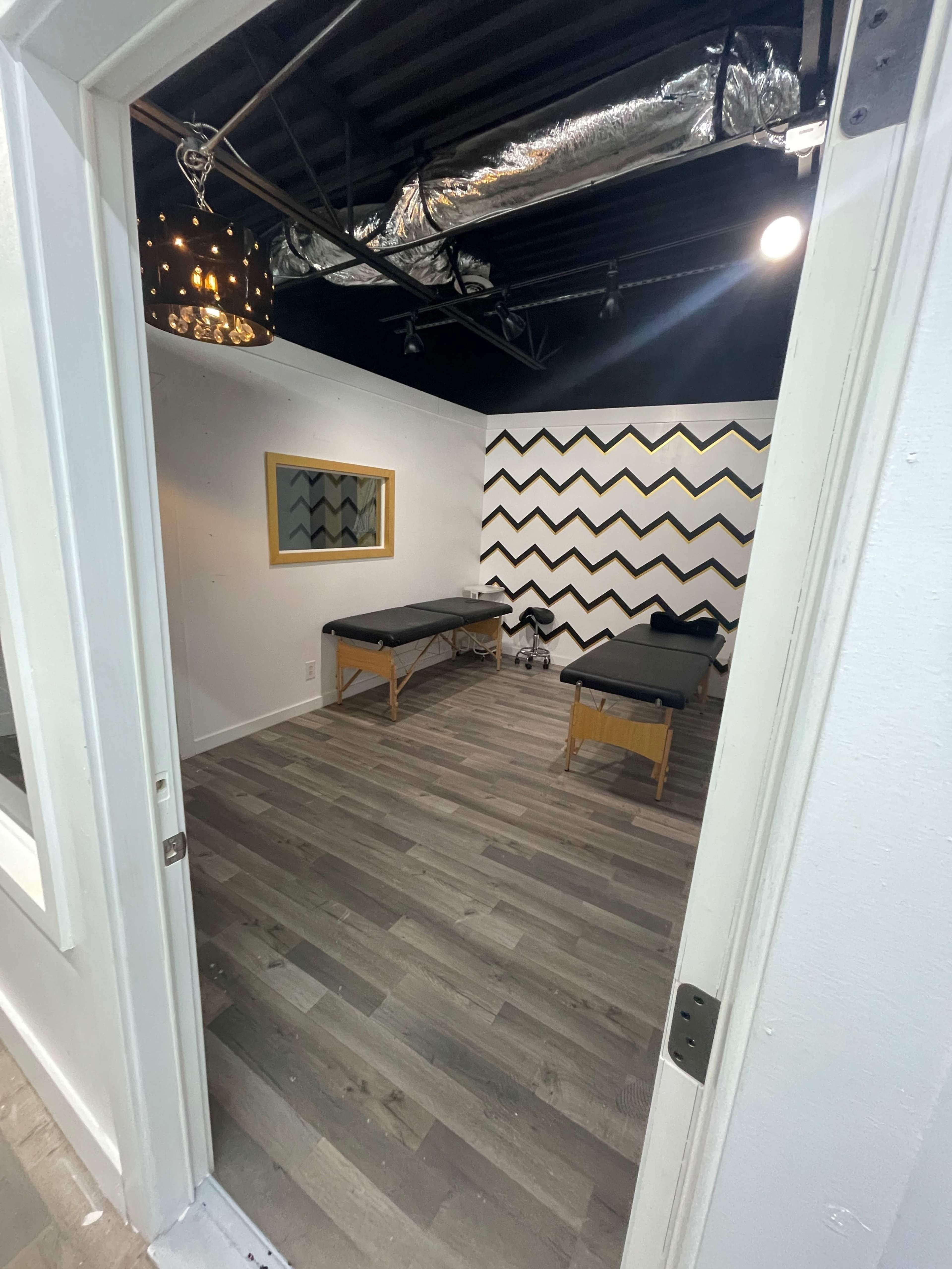 A room with two treatment tables, a striped accent wall, and a mirror.