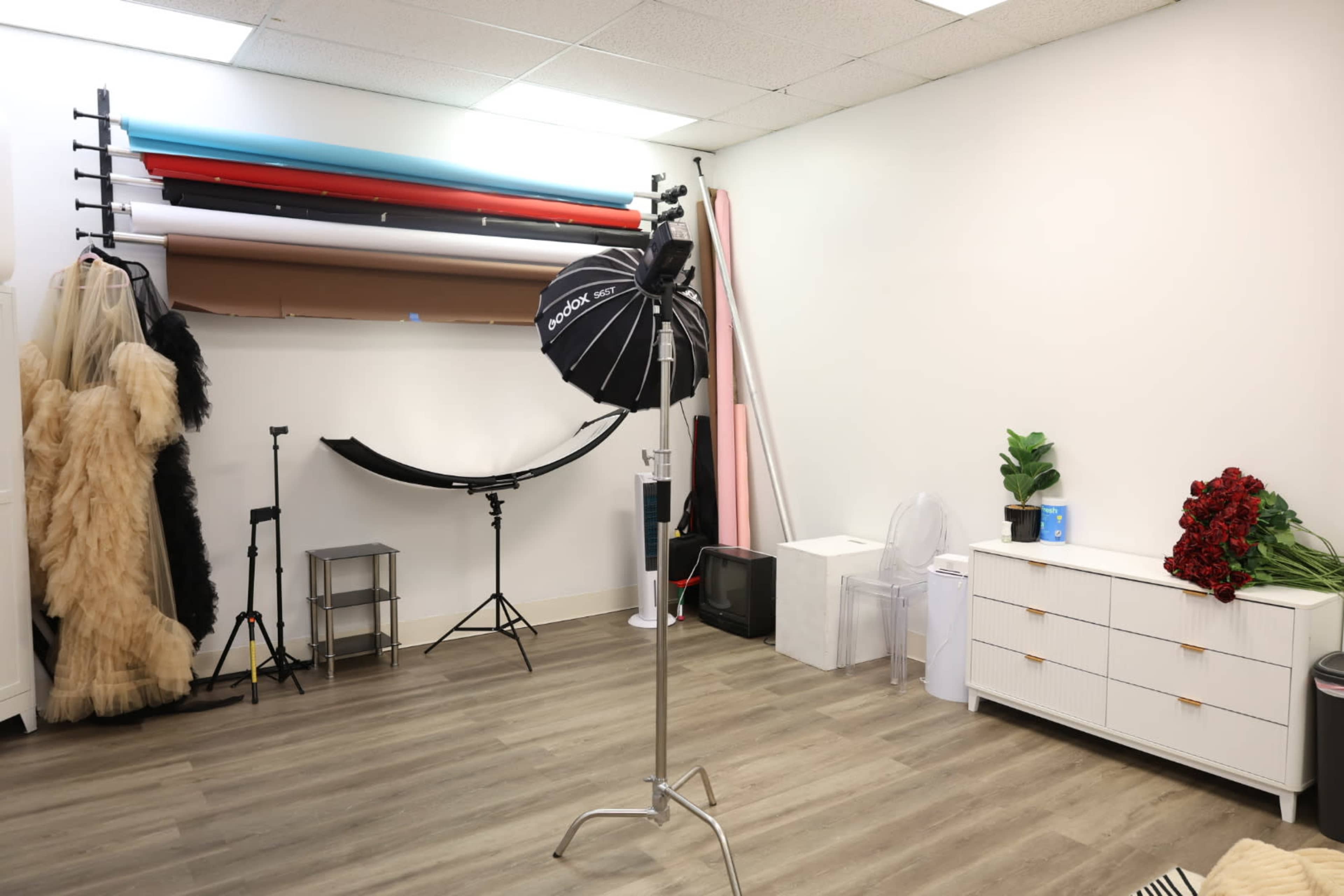 The image shows a spacious studio with various backdrops, a light stand, and a neatly arranged cabinet, complemented by props such as a bouquet of red roses.