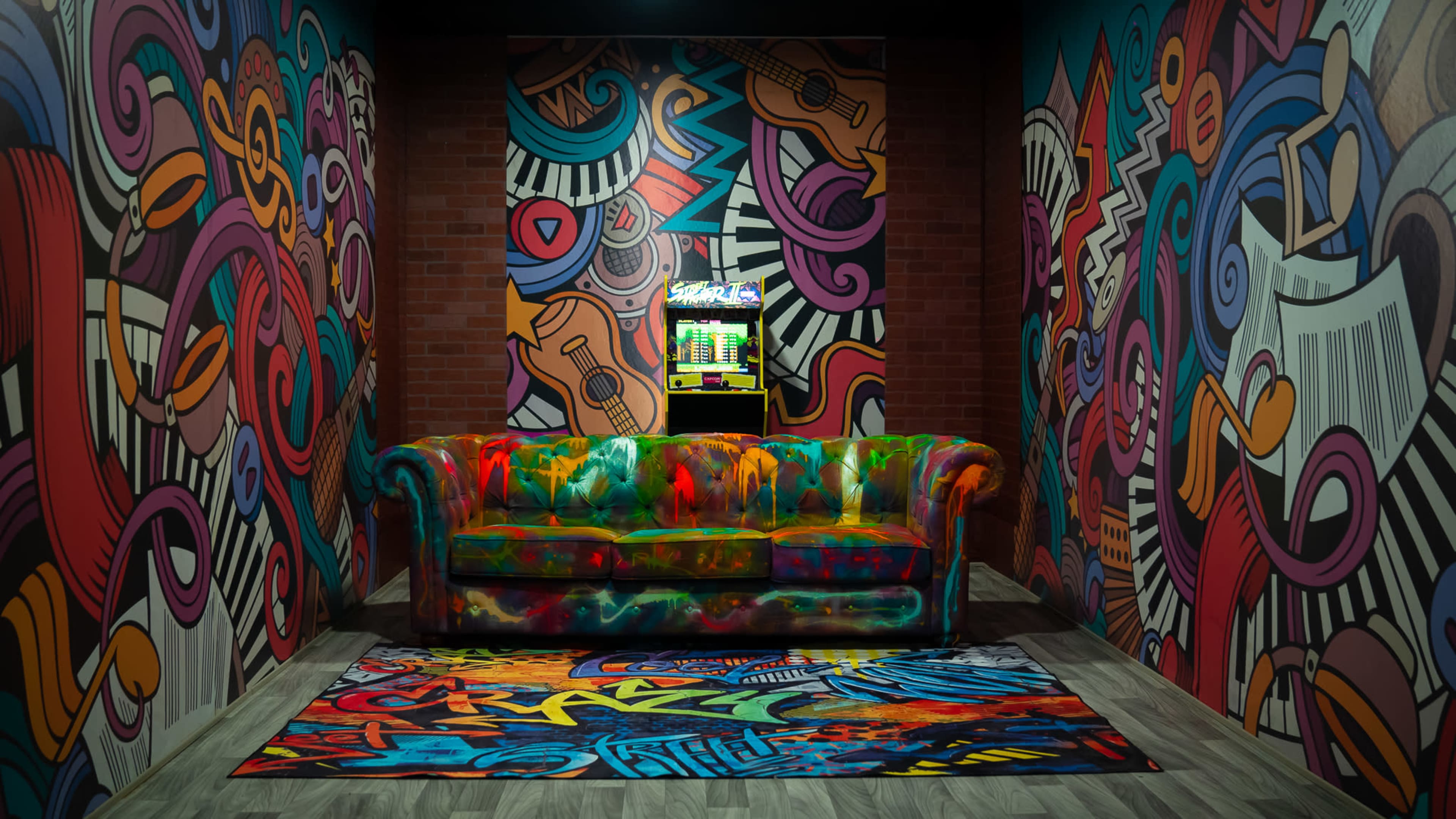 The scene features a vibrant, graffiti-covered room with a colorful couch and a patterned rug, all surrounded by eclectic wall art and a small arcade machine.