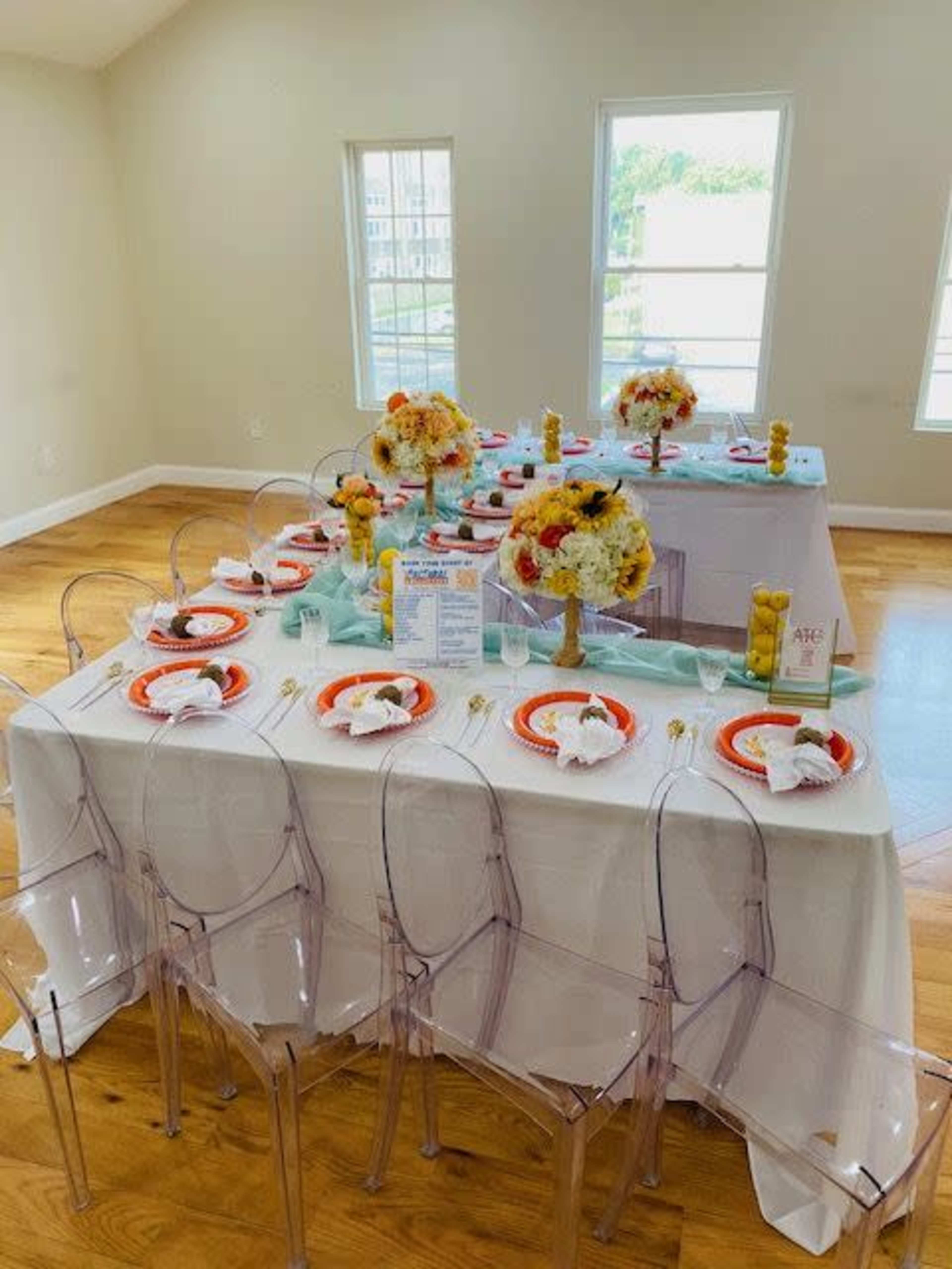 A neatly arranged dining table with colorful tableware and floral centerpieces is set in a well-lit room with large windows.