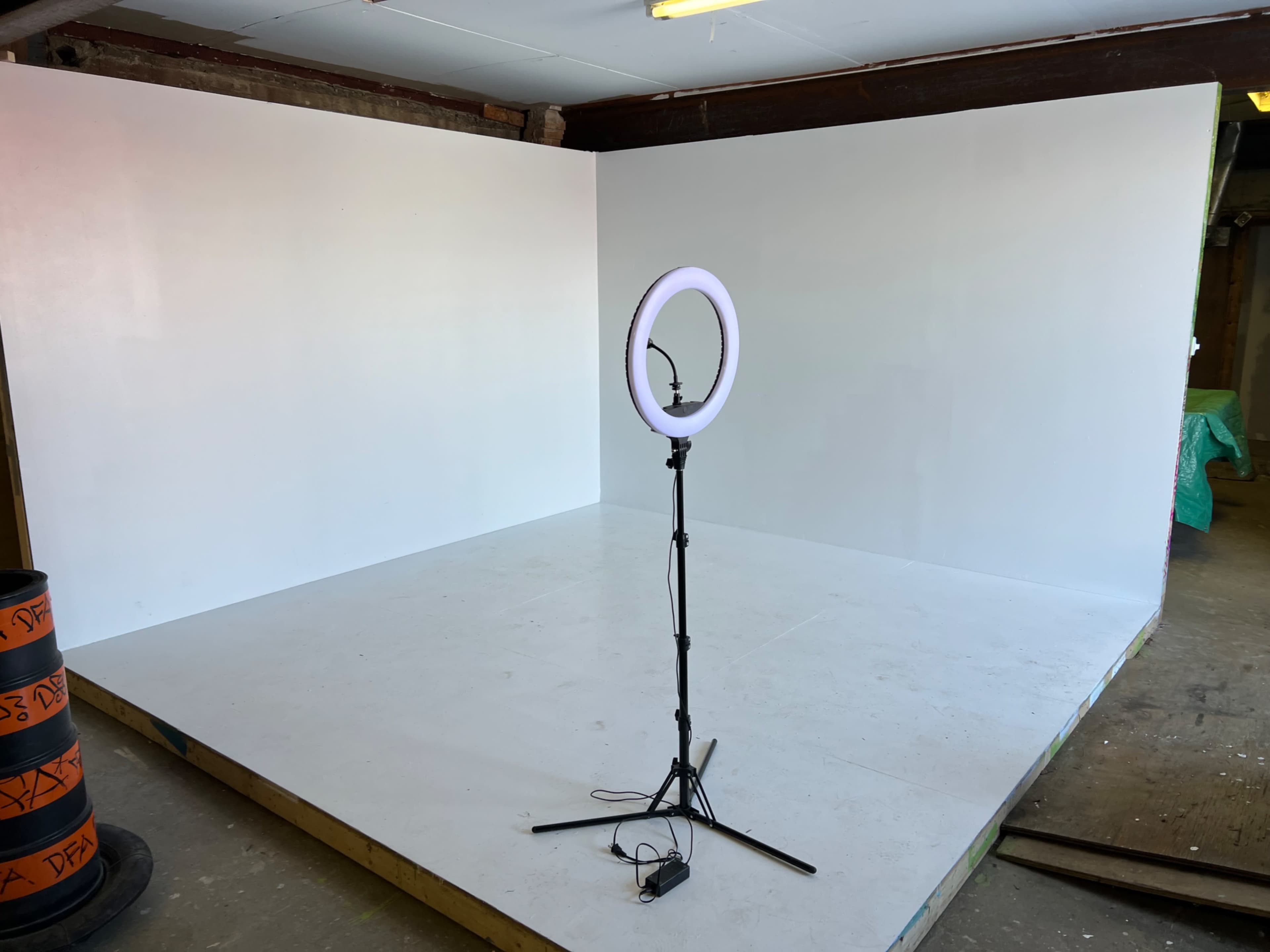 A simple, empty room with a white backdrop and a ring light set on a tripod in one corner.