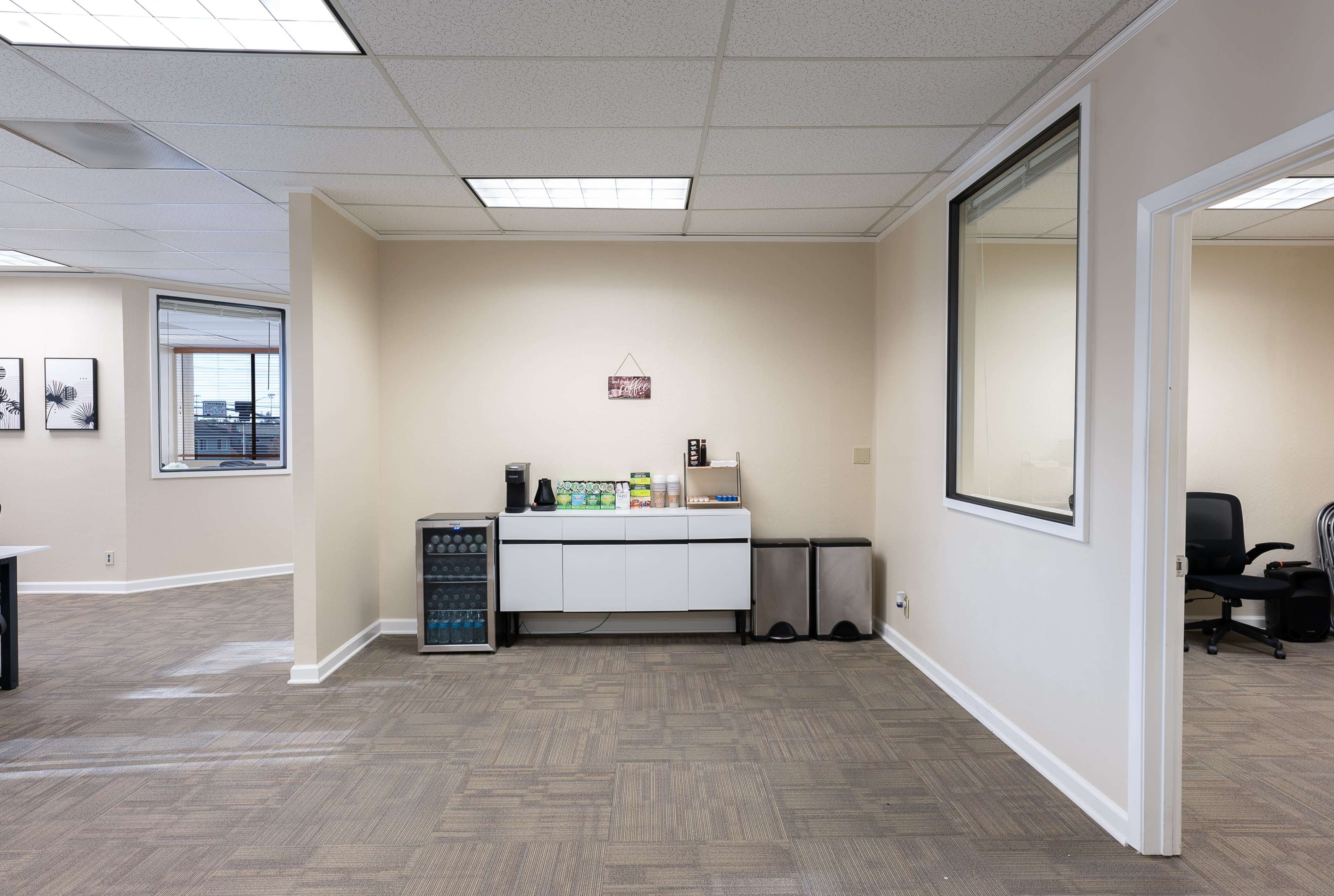 The image shows a light-colored office space with a cabinet and appliances against a wall, and an empty workstation in the corner.