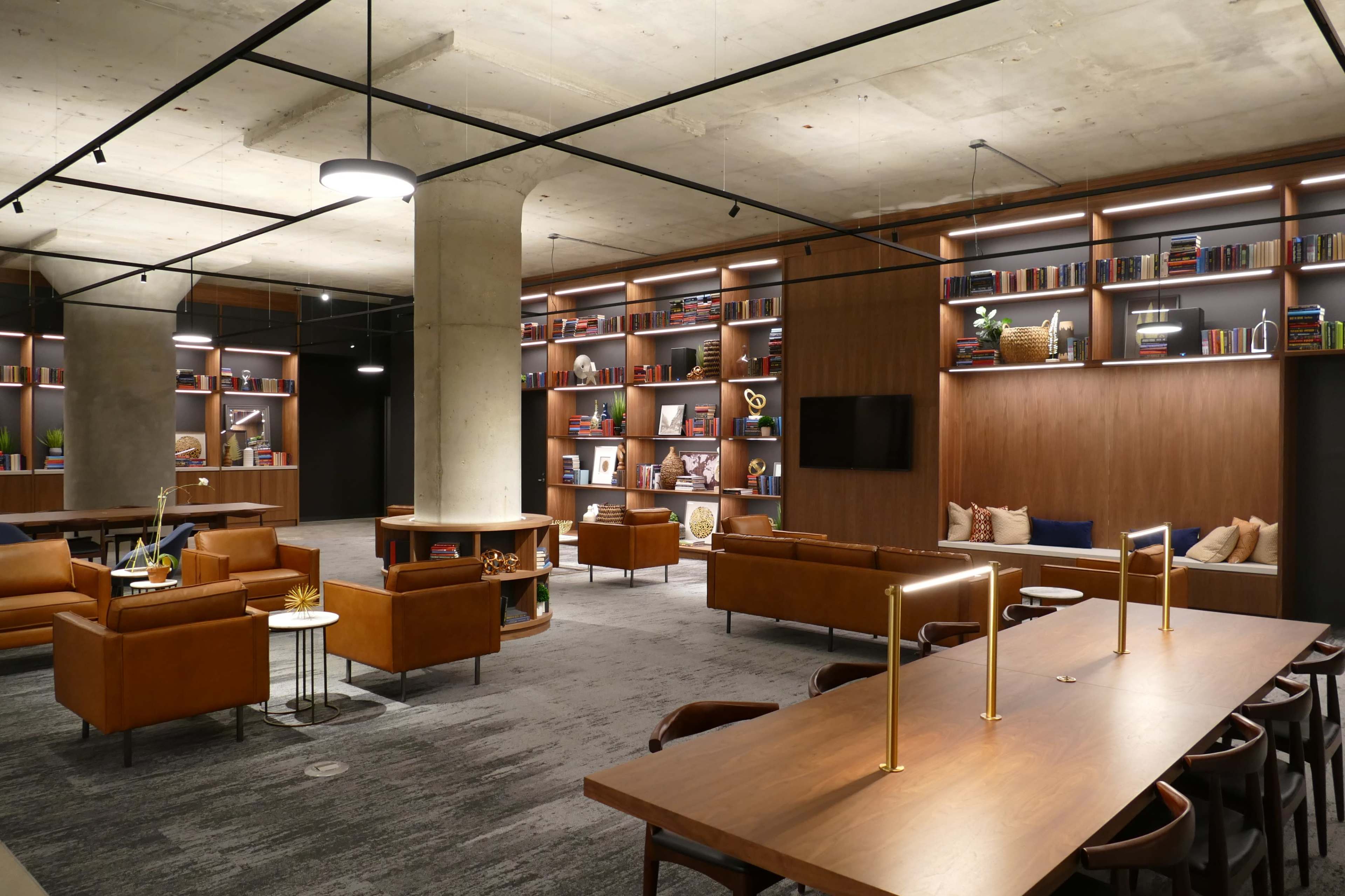 A modern lounge area with leather seating, wooden tables, and shelves filled with books.
