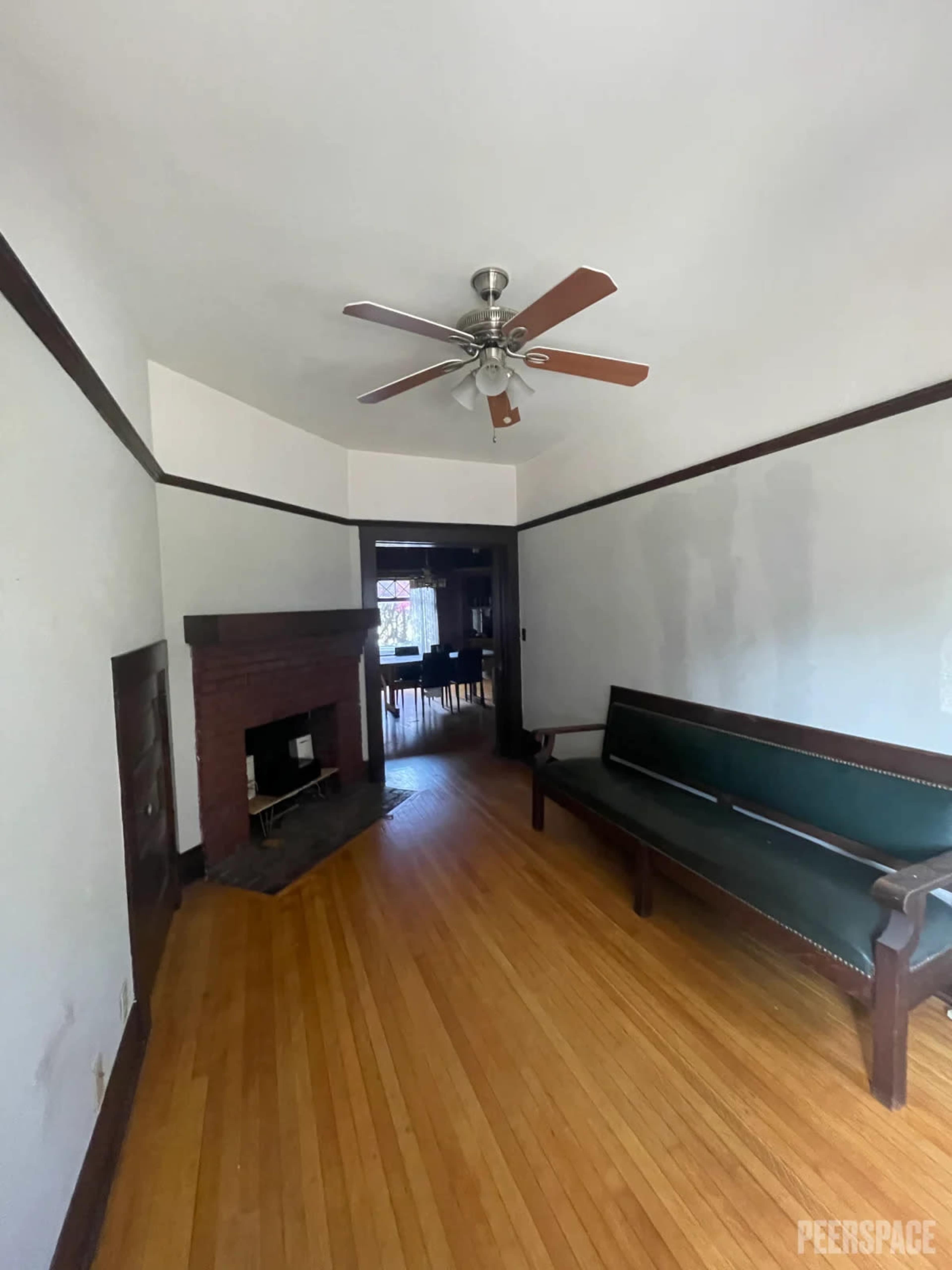 A hallway leading to a room with a wooden floor, a ceiling fan, and a fireplace.