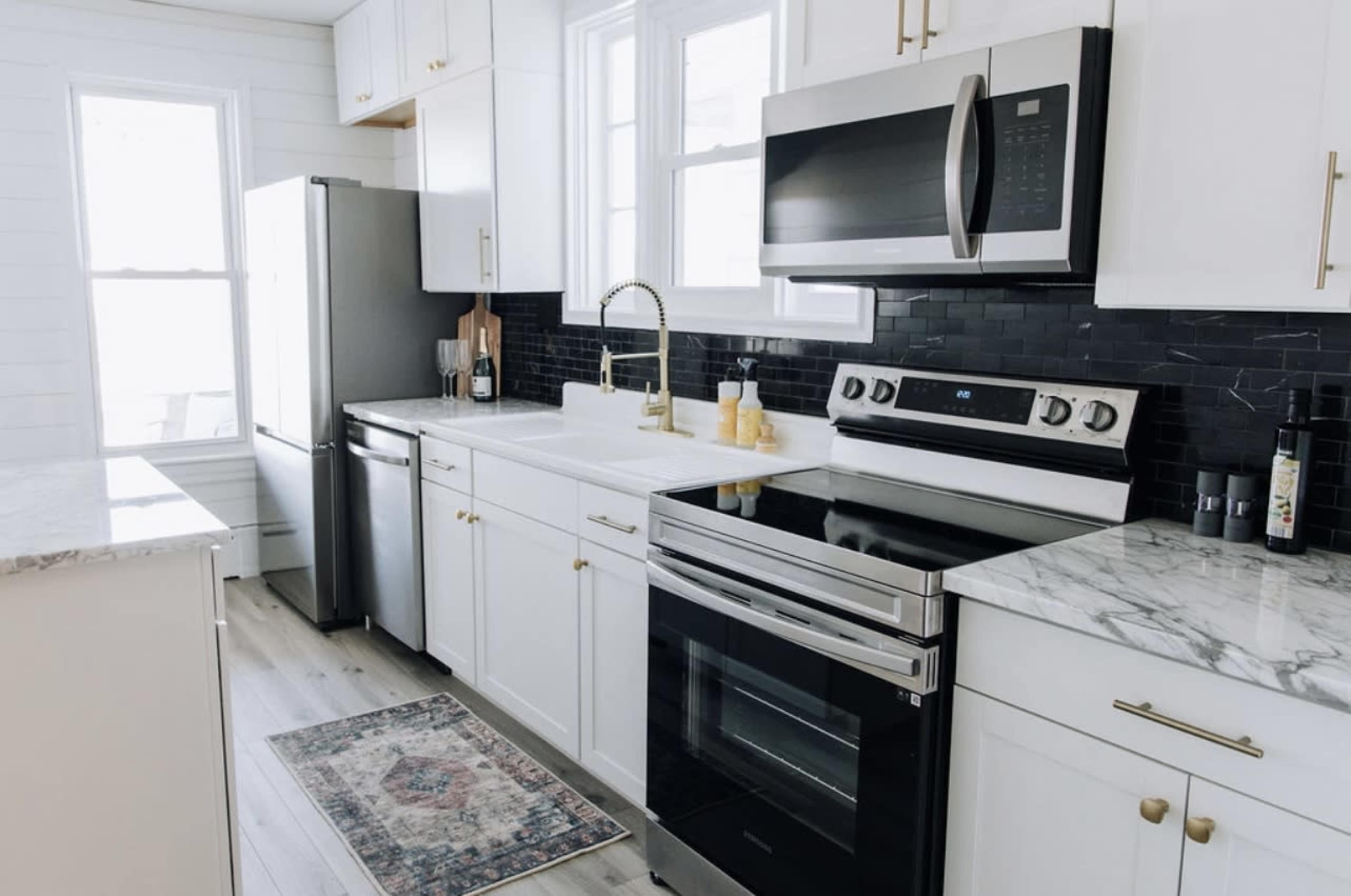 A modern kitchen features white cabinetry, stainless steel appliances, a marble countertop, and a patterned rug on the floor.