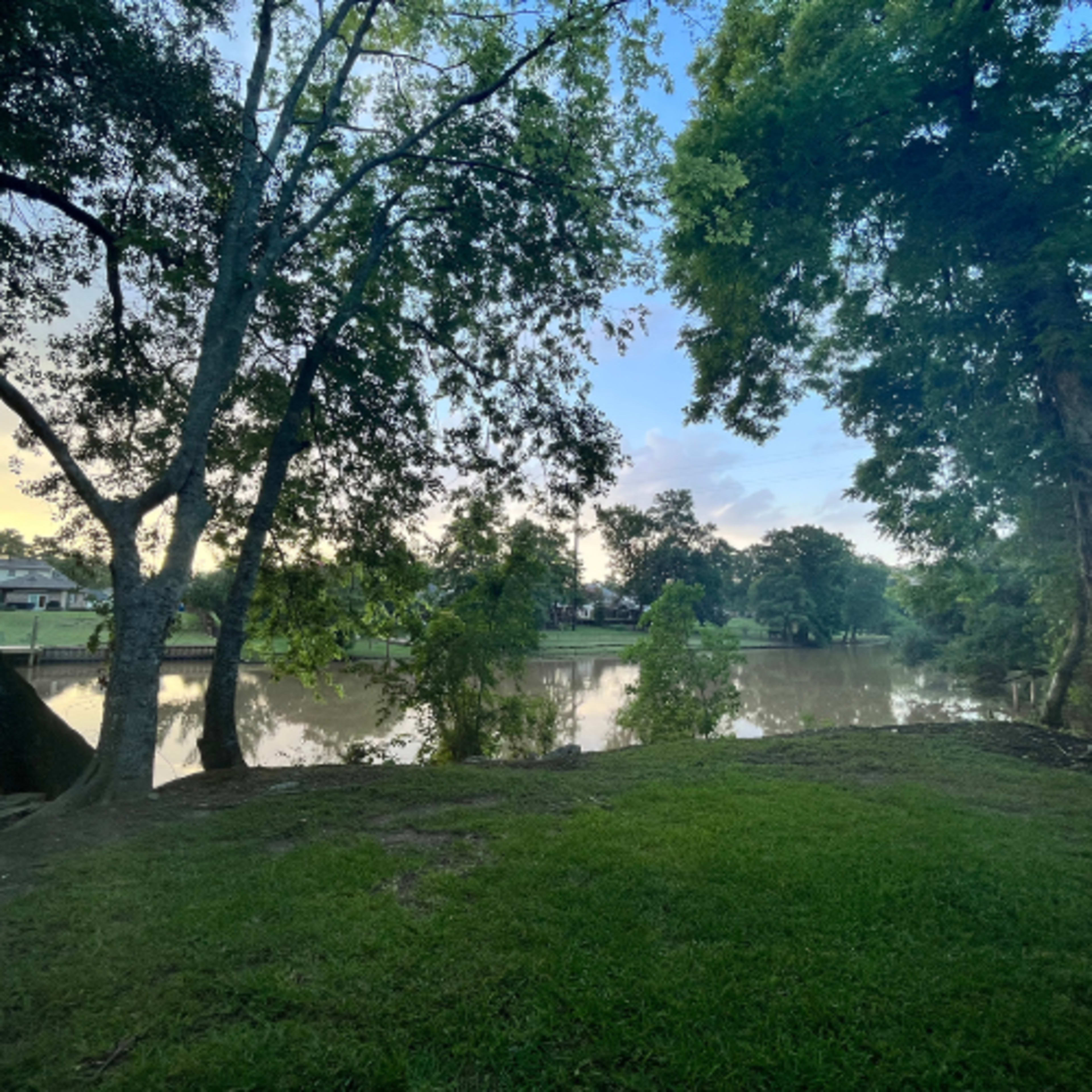 The scene features a calm river bordered by trees and lush greenery under a clear sky.