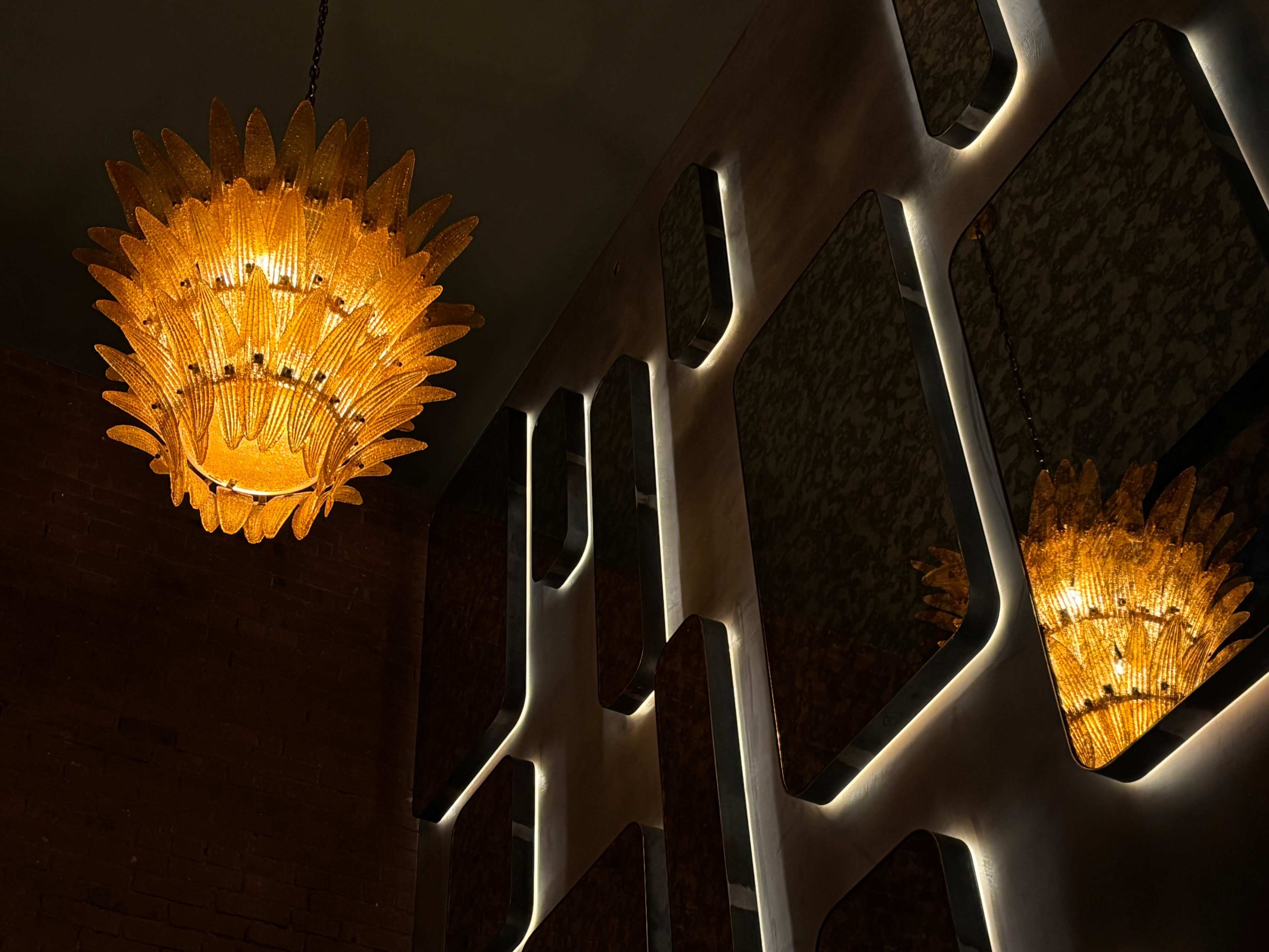 A large, star-shaped chandelier with amber glass adorns a wall featuring abstract, mirrored panels that reflect light.
