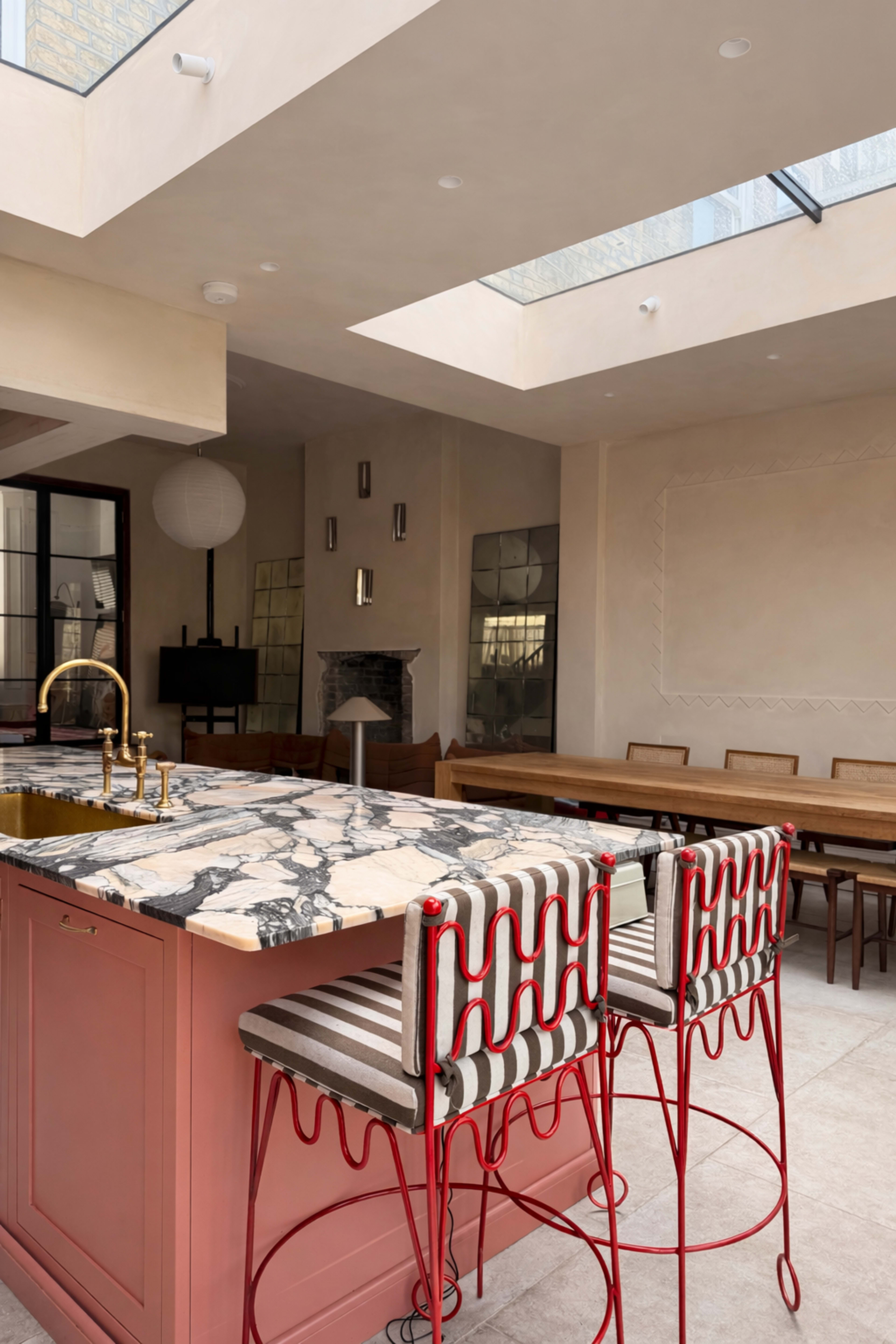The image features a modern kitchen with a marble-topped island, red bar stools, and a spacious dining area illuminated by natural light from a skylight.