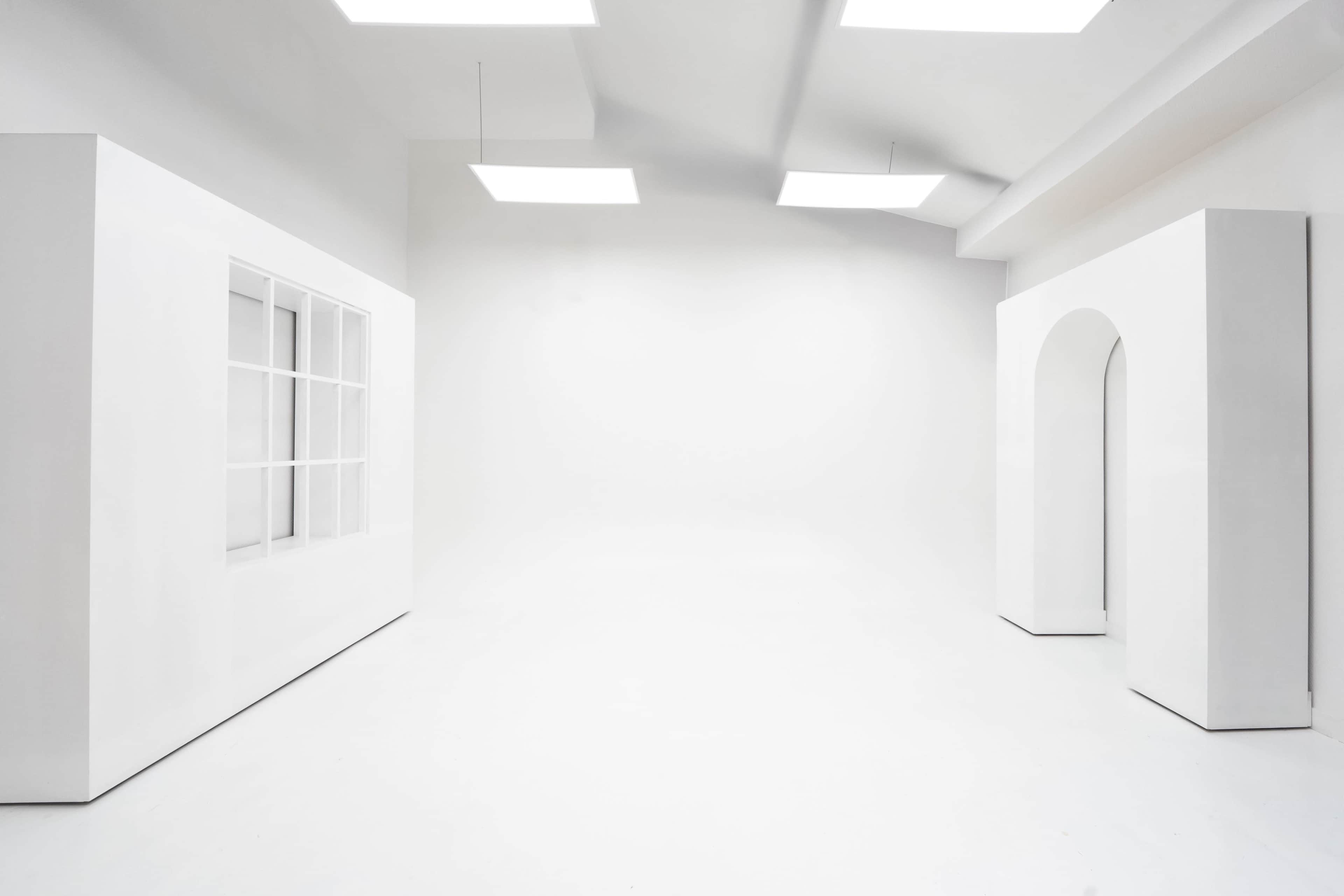 The image shows a minimalist, white interior space featuring a window with multiple panes and an archway.