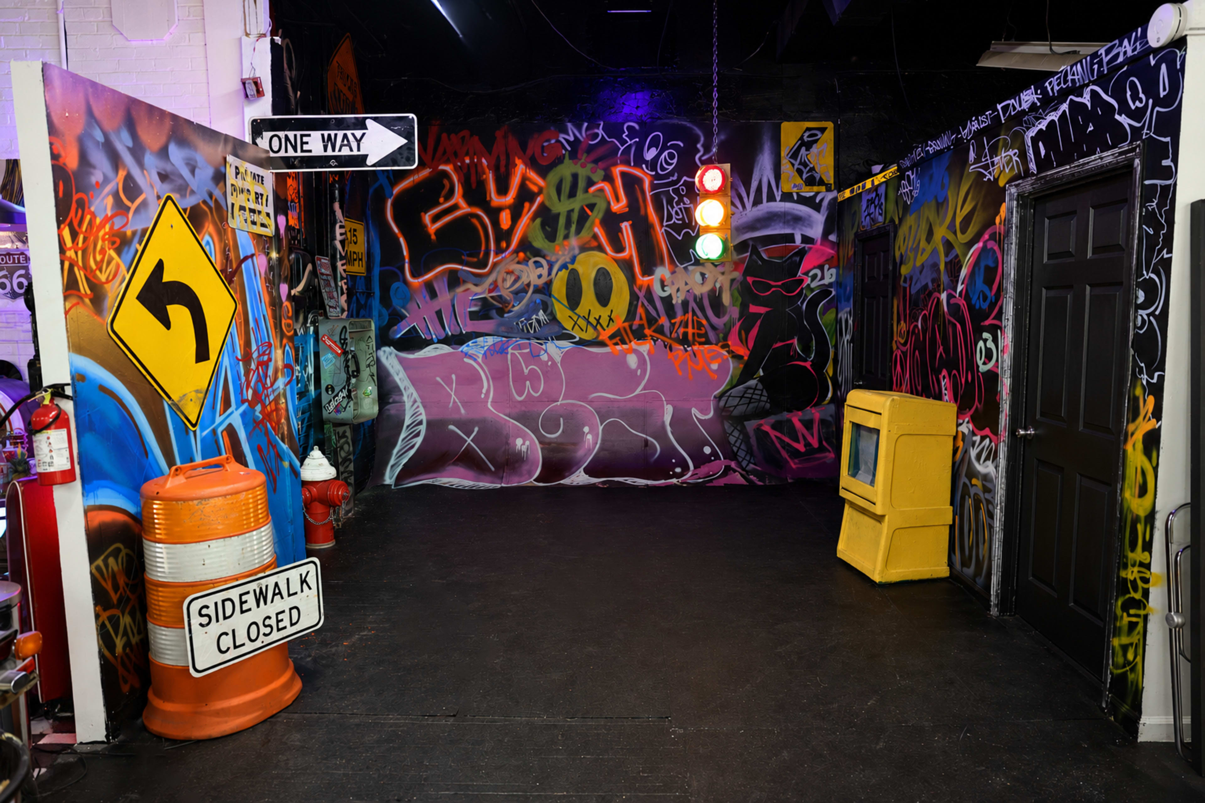 The scene features a graffiti-covered urban space with traffic signs, a yellow trash can, and a closed sidewalk sign.