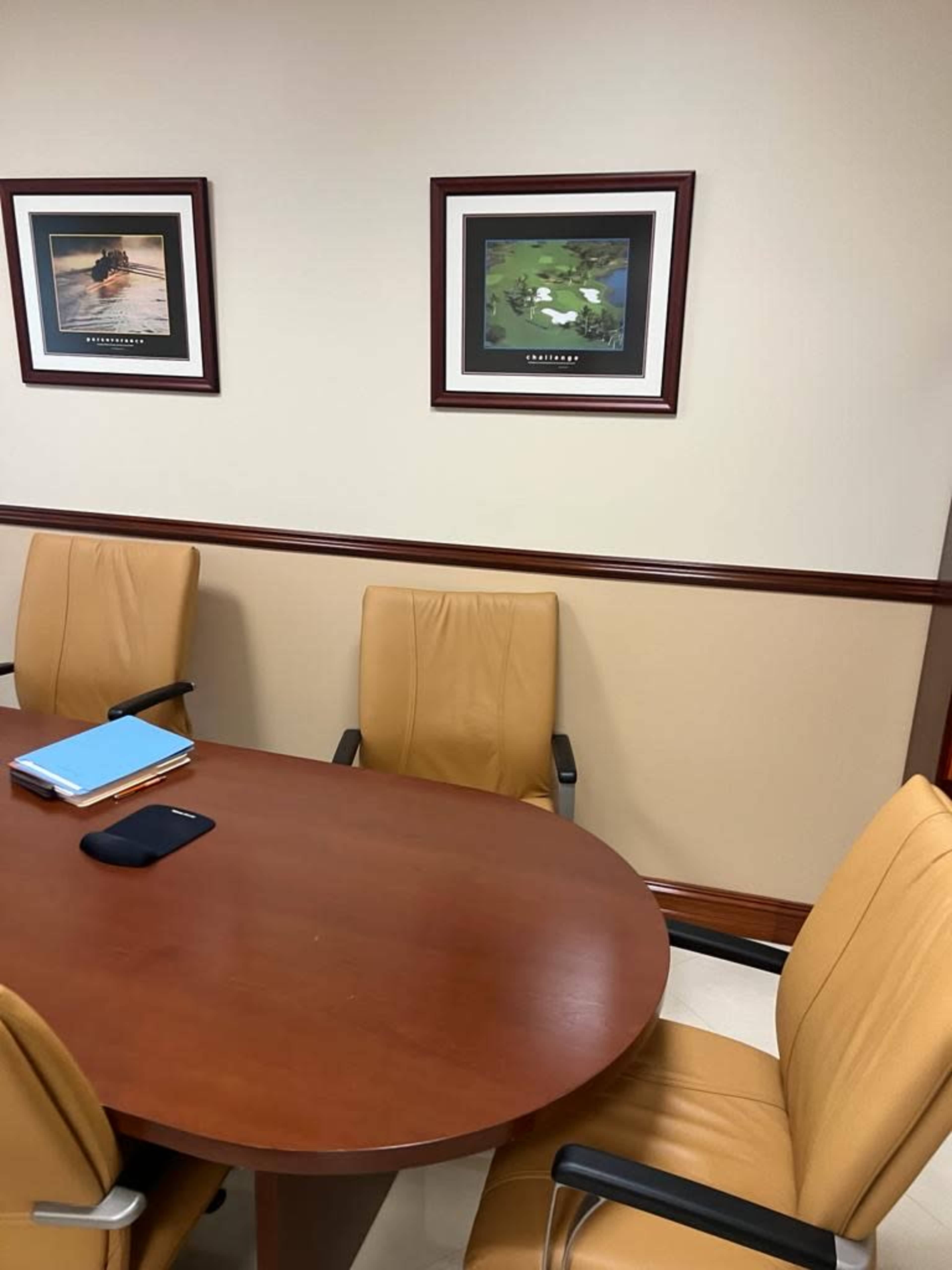 A conference room with a round wooden table, yellow chairs, and framed artwork on the walls.
