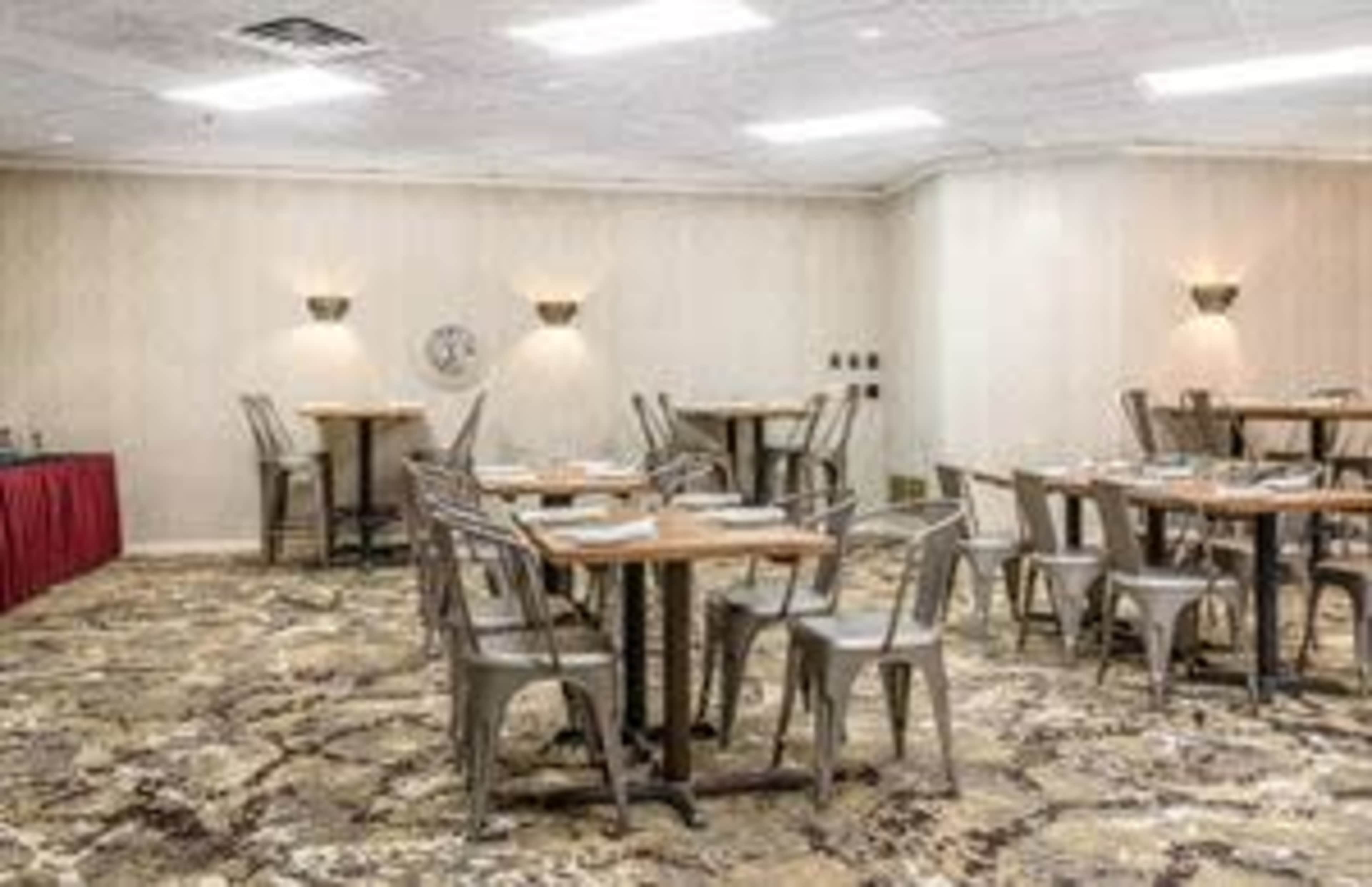 The image shows a dining area with several tables and metal chairs arranged on a patterned carpet.