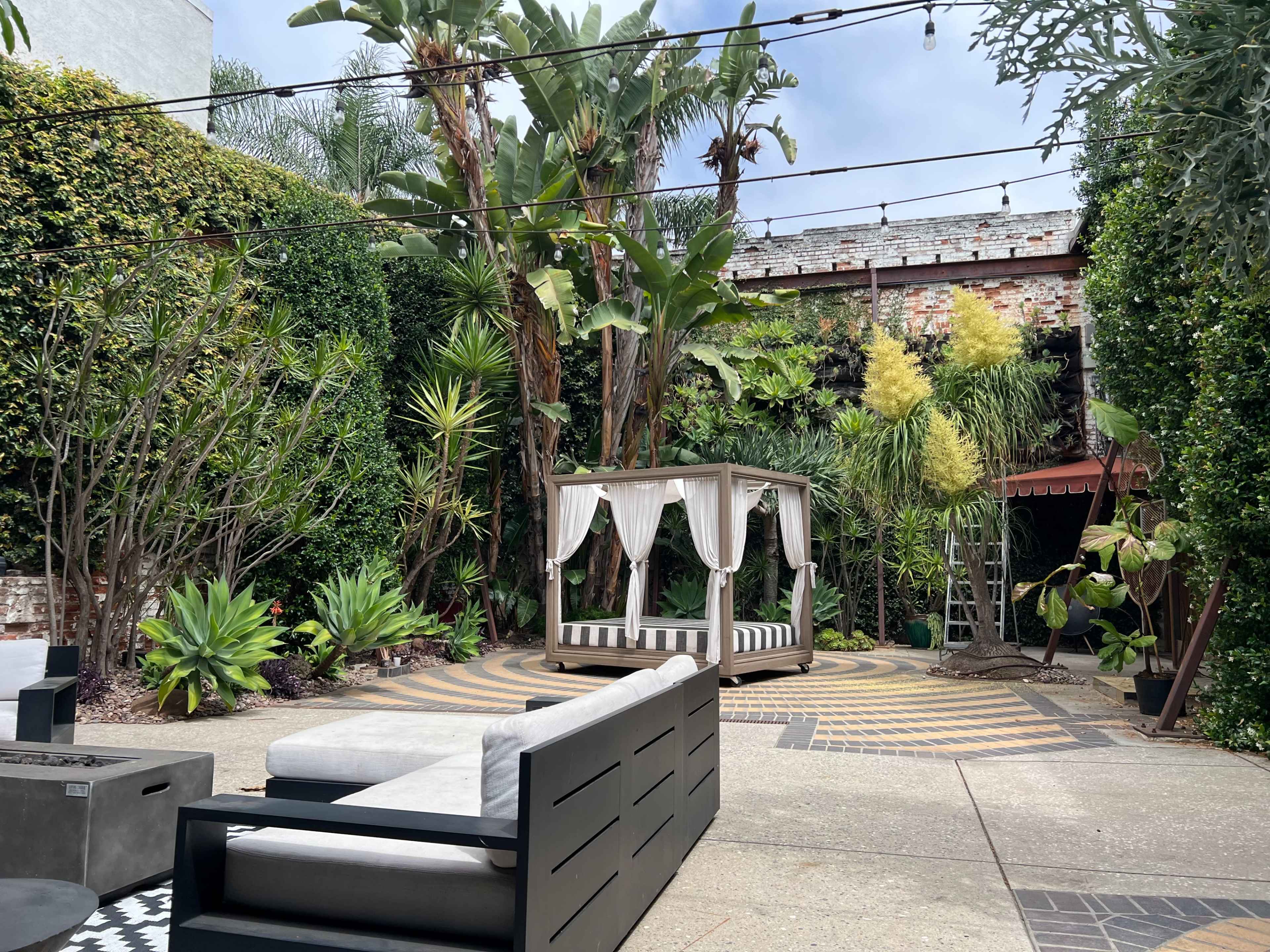 The image features a landscaped garden with a seating area, a gazebo, and various tropical plants surrounded by brick walls.