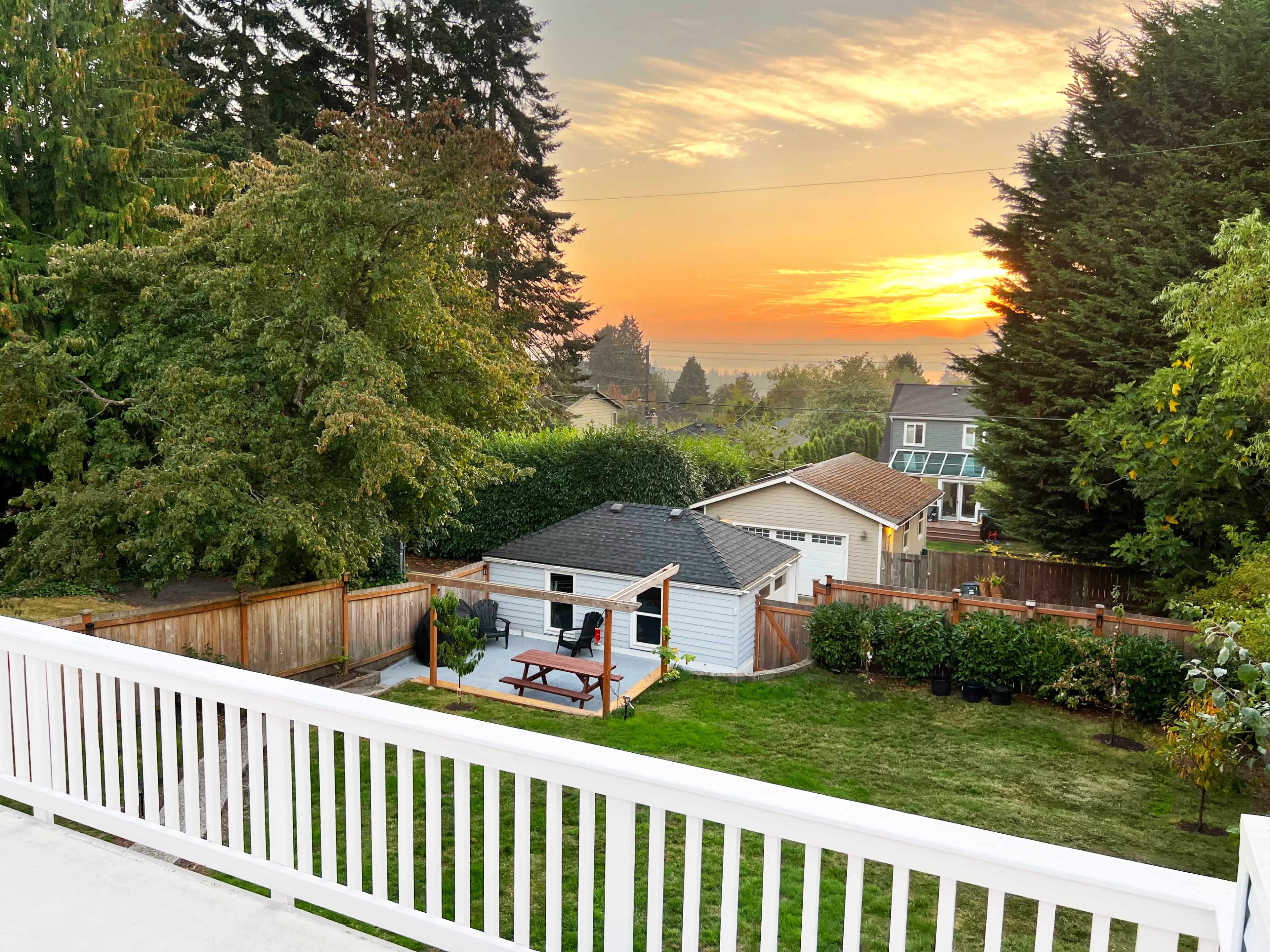A backyard with a picnic table and a shed, framed by trees, as the sun sets in the background.