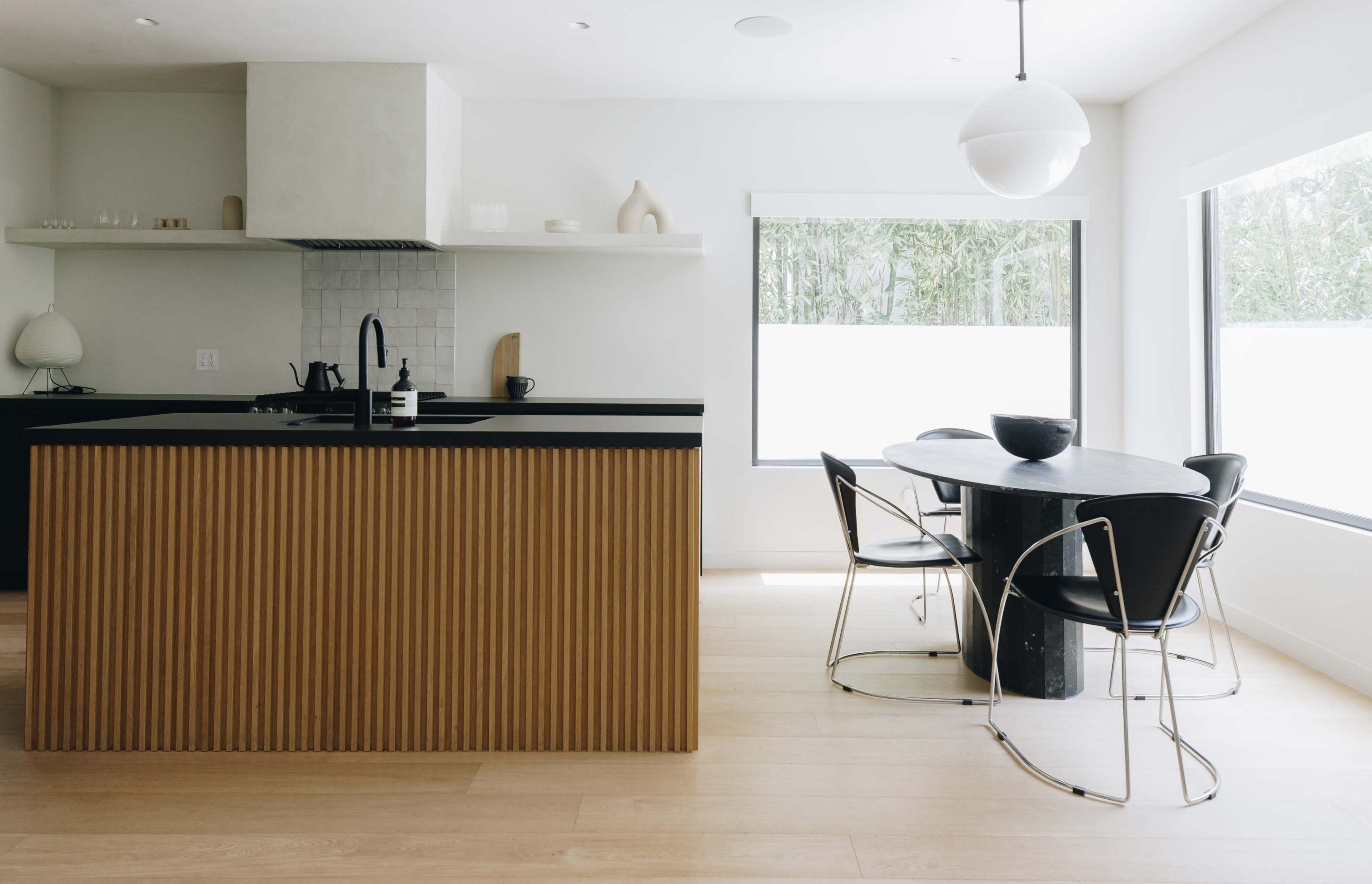 A modern kitchen with an island featuring a ribbed wooden front and a round dining table surrounded by black chairs.