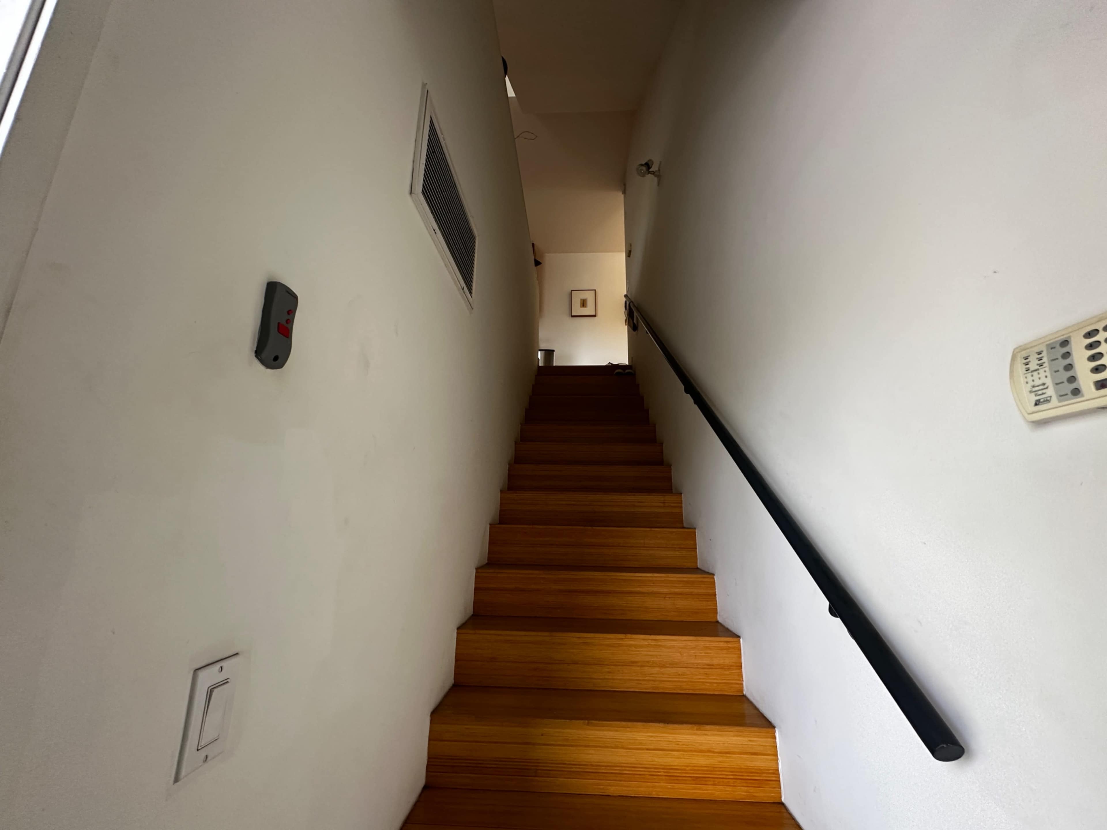 A narrow staircase with wooden steps leads upward in a well-lit hallway.