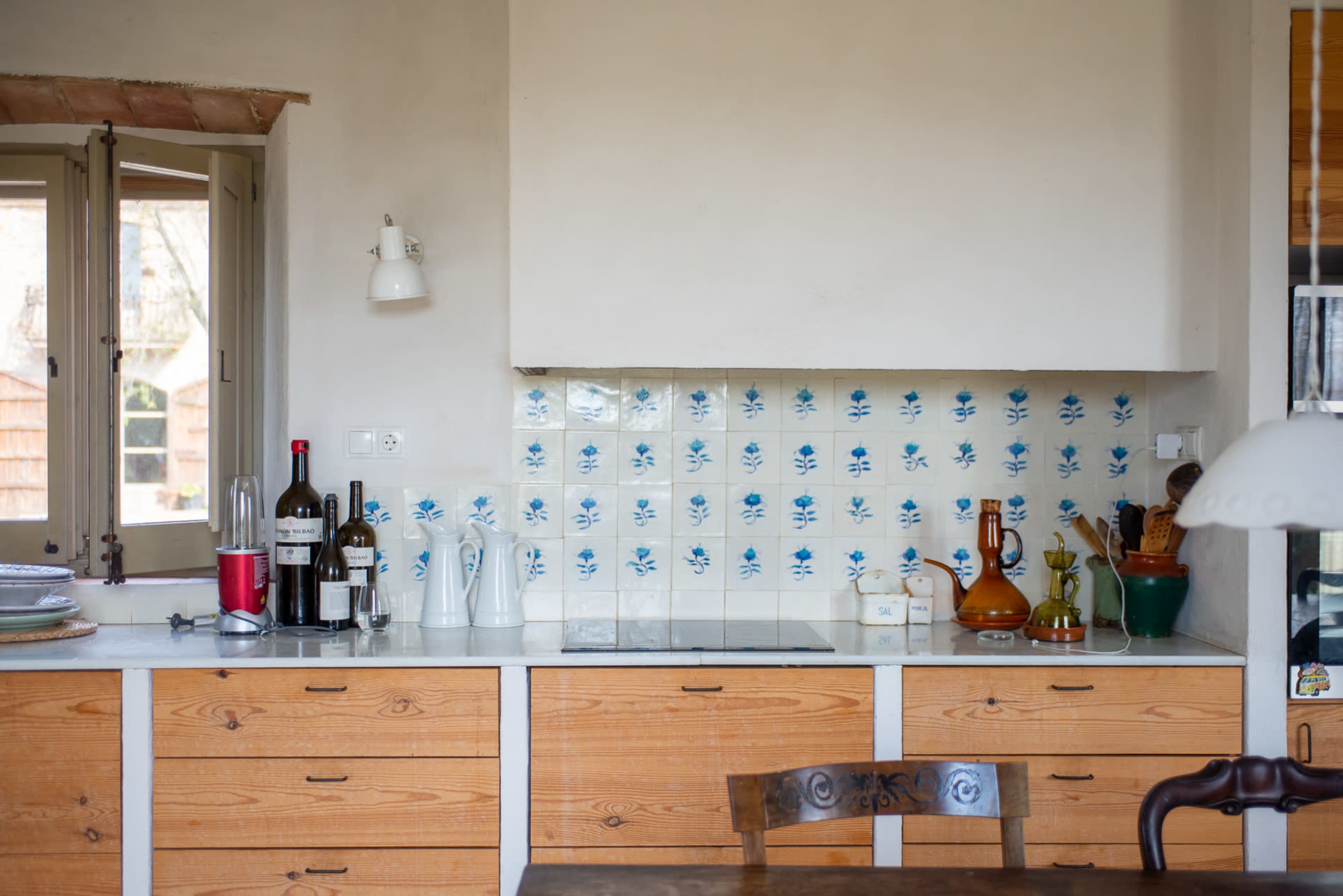 A kitchen with wooden cabinets, a white countertop, and blue floral tiles on the wall, along with various kitchen items and bottles on display.