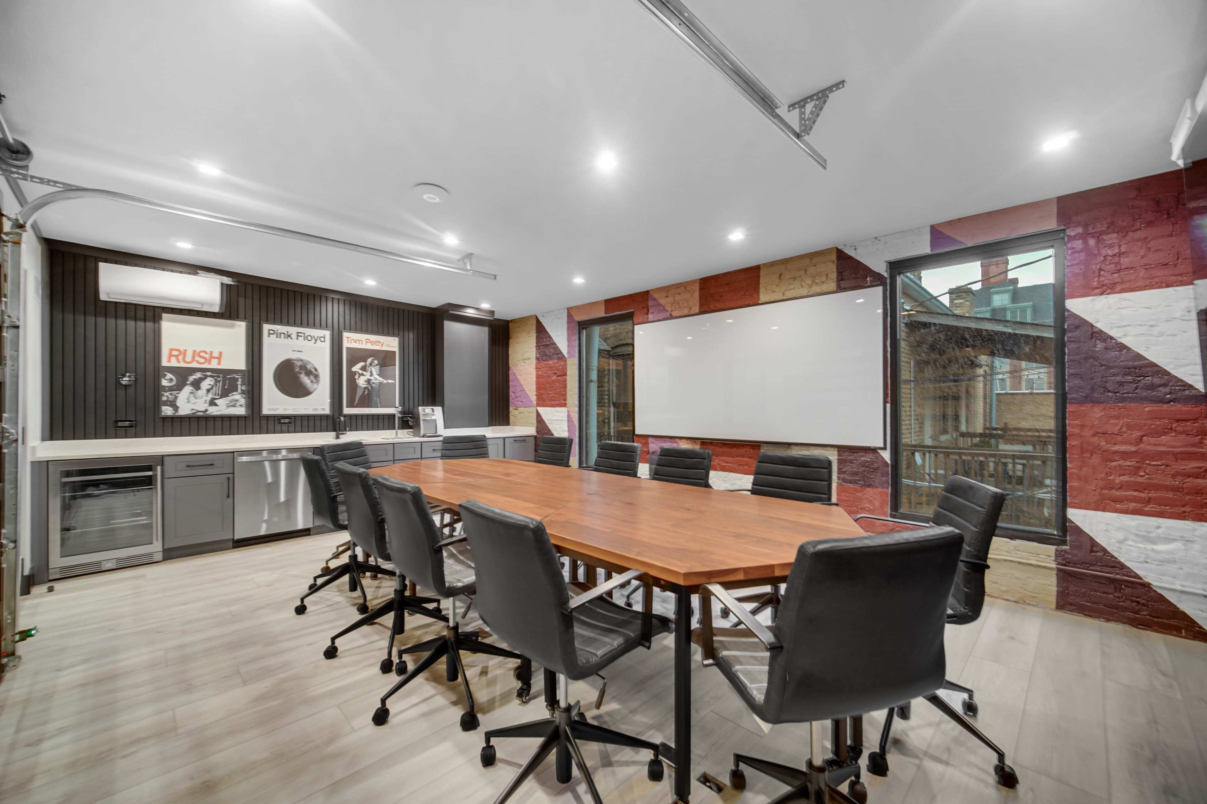 The image shows a modern conference room with a large wooden table surrounded by black chairs and colorful wall art.