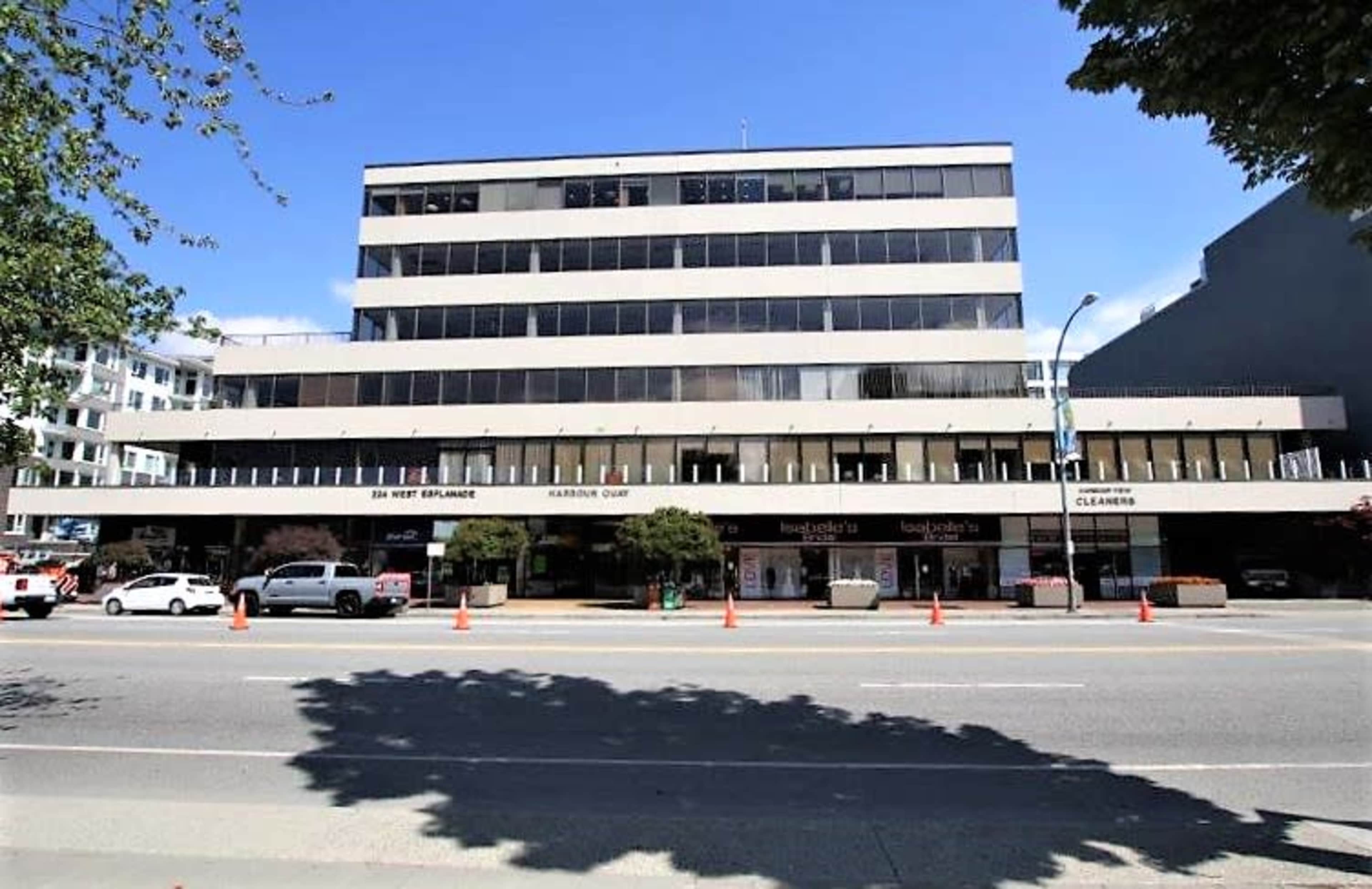 The image shows a multi-story commercial building with a flat façade, located on a busy street lined with vehicles and orange traffic cones.