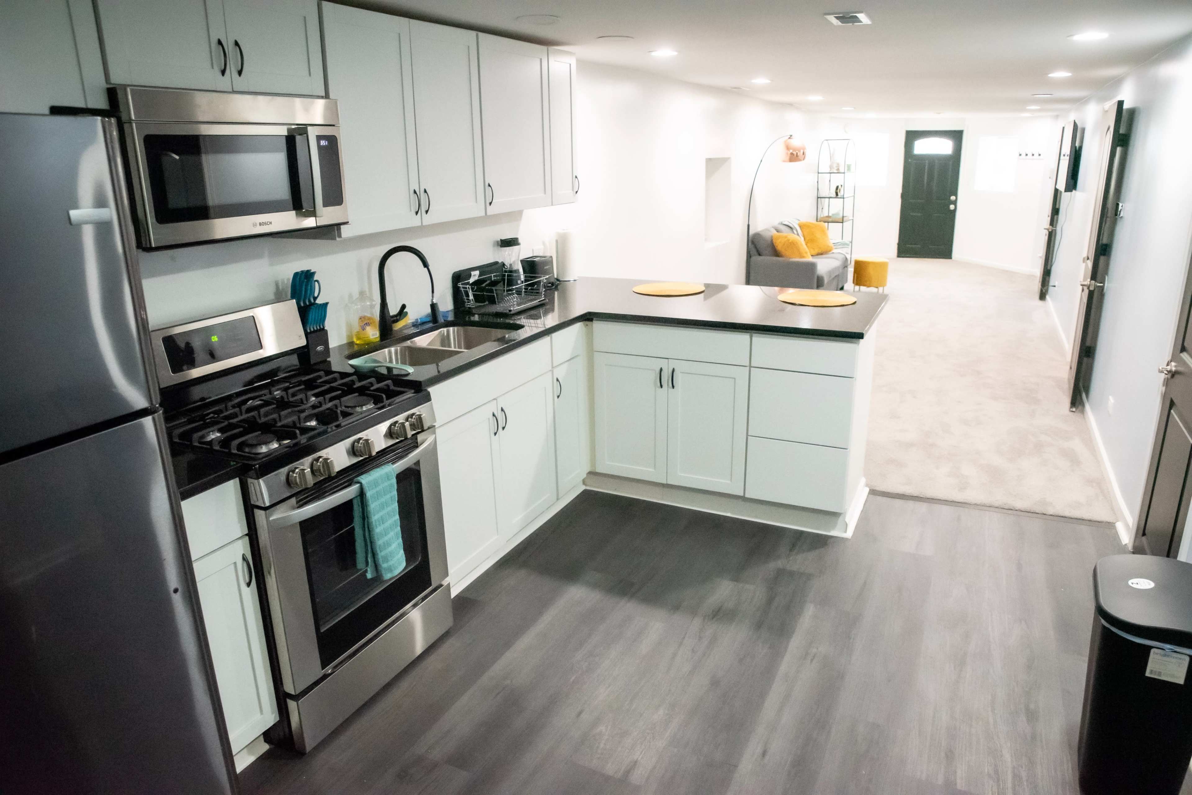 A modern kitchen area with stainless steel appliances, including a gas stove, alongside a dining space featuring a gray sofa in a well-lit corridor.
