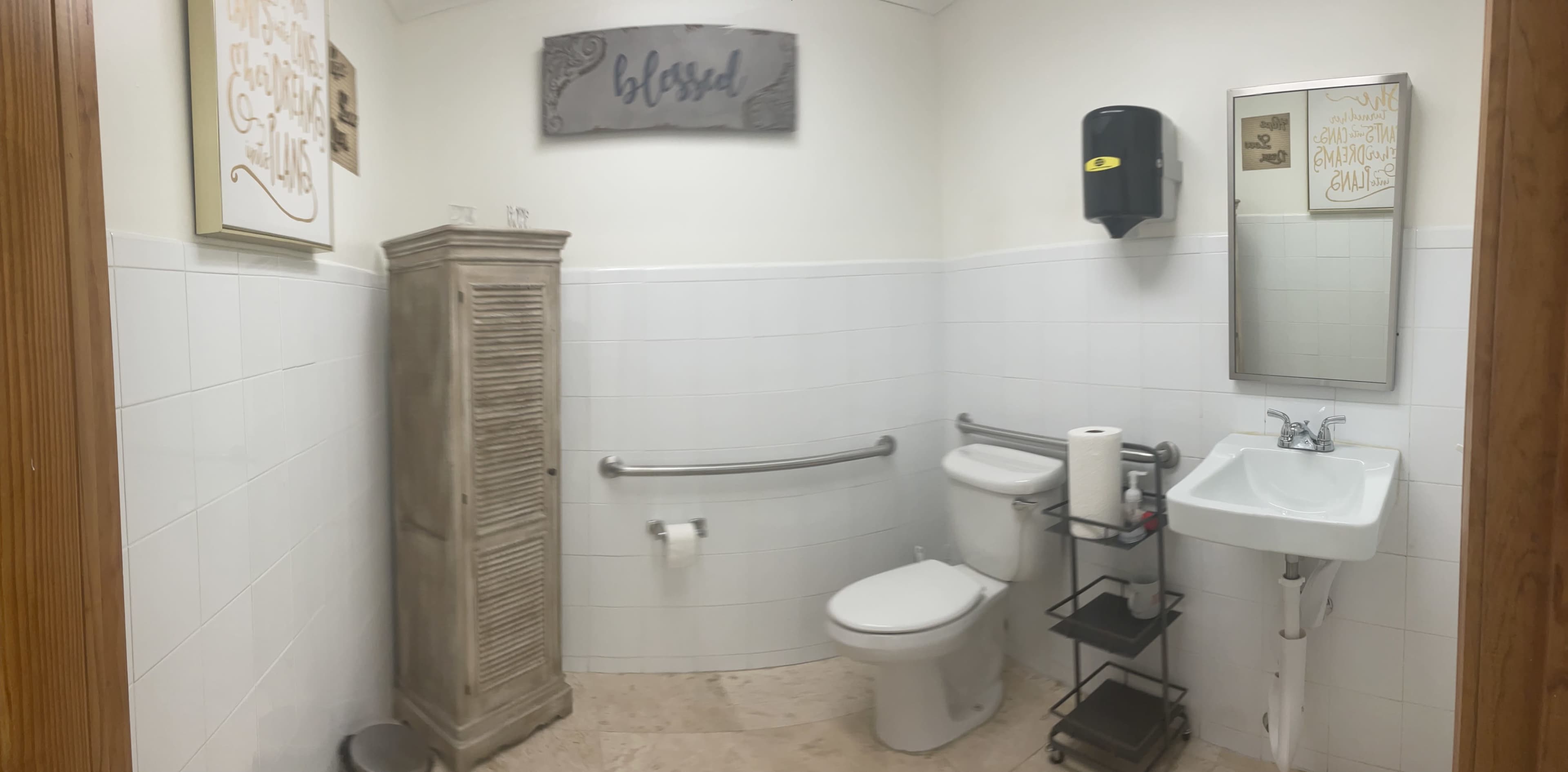 A clean, well-lit bathroom featuring a toilet, sink, storage cabinet, and a wall-mounted paper towel dispenser.