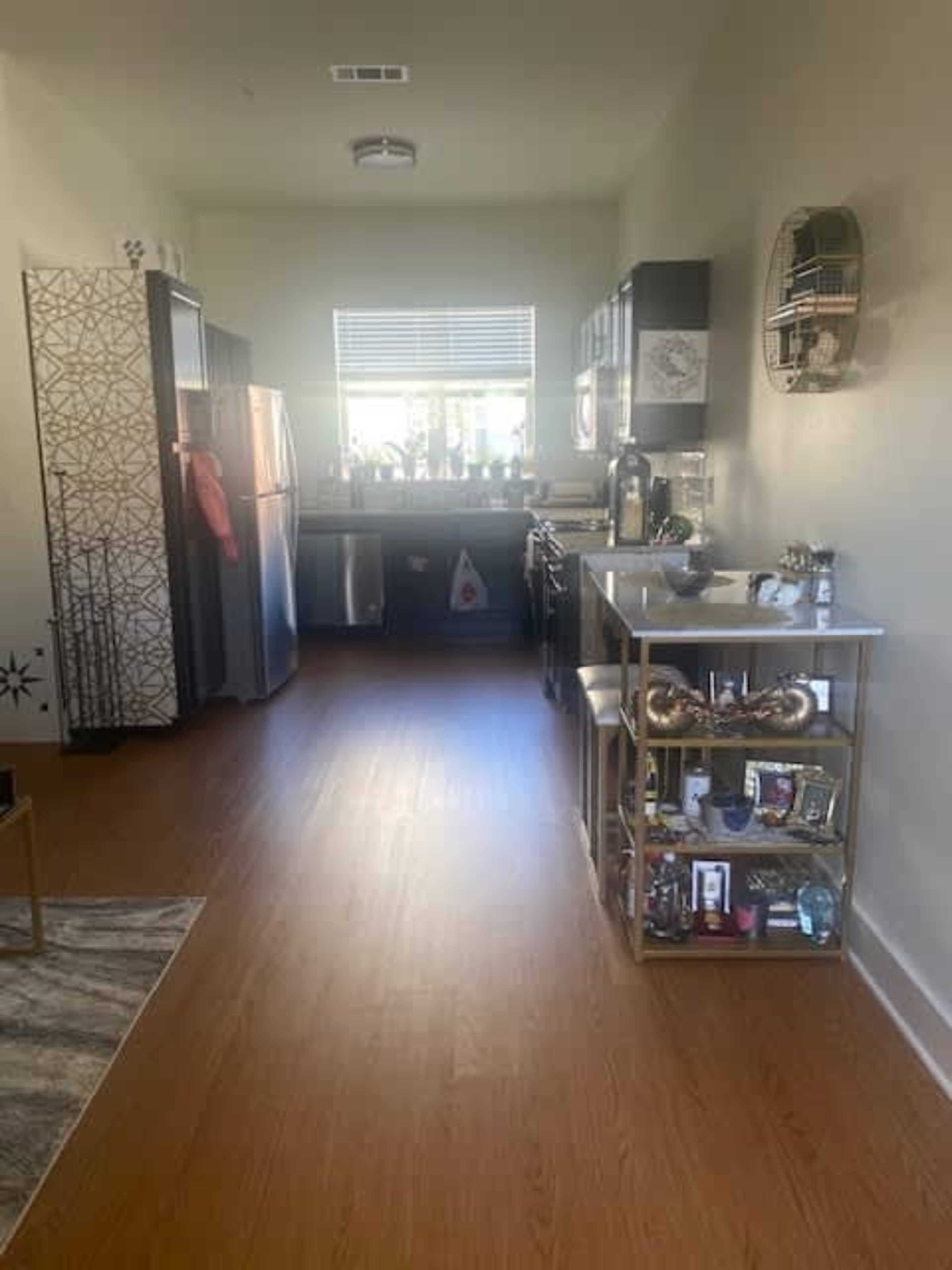 The image shows a kitchen with stainless steel appliances, a countertop with various items, and wooden flooring.