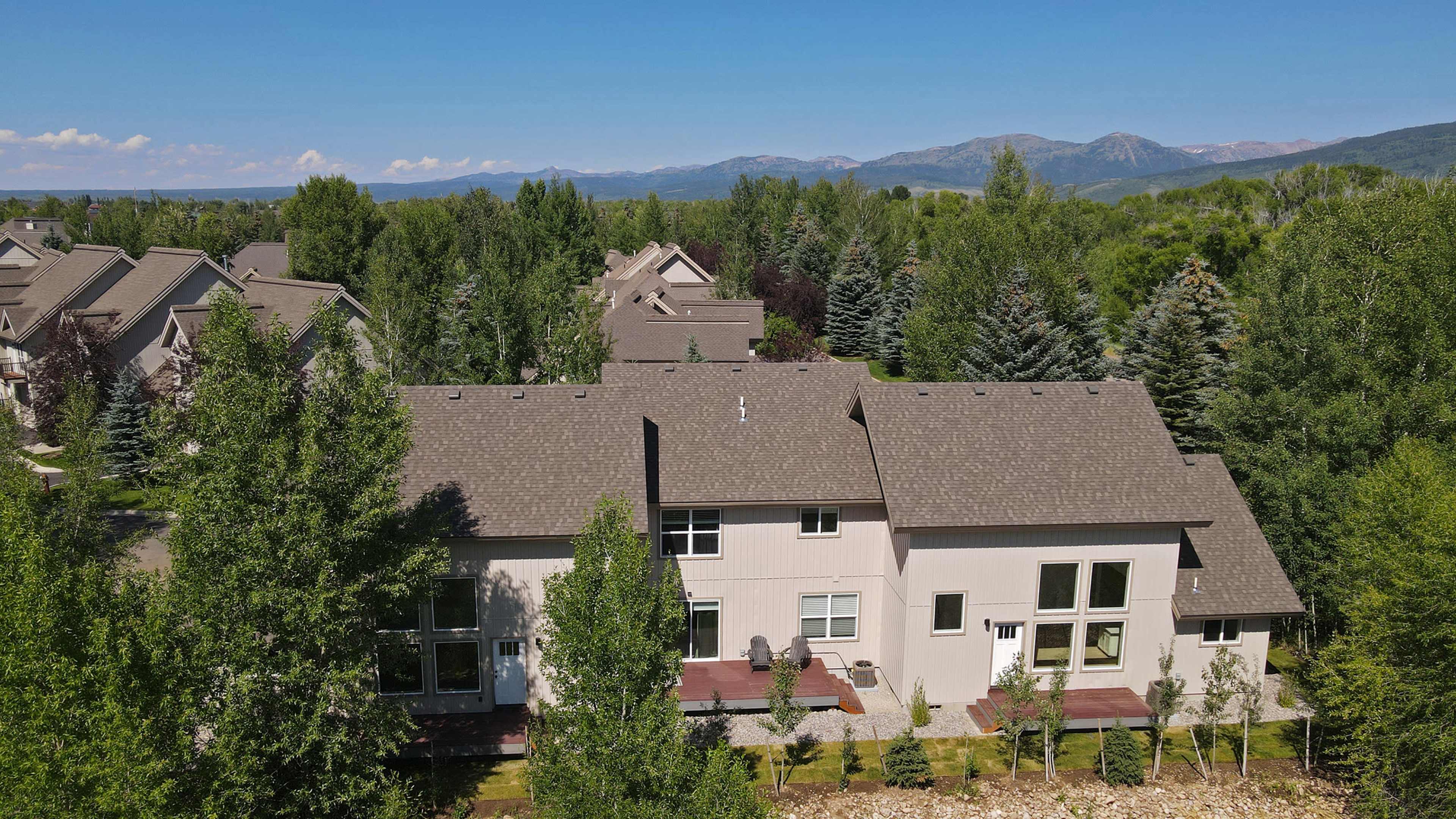 Aerial view of a modern residential neighborhood surrounded by trees and mountains in the background.