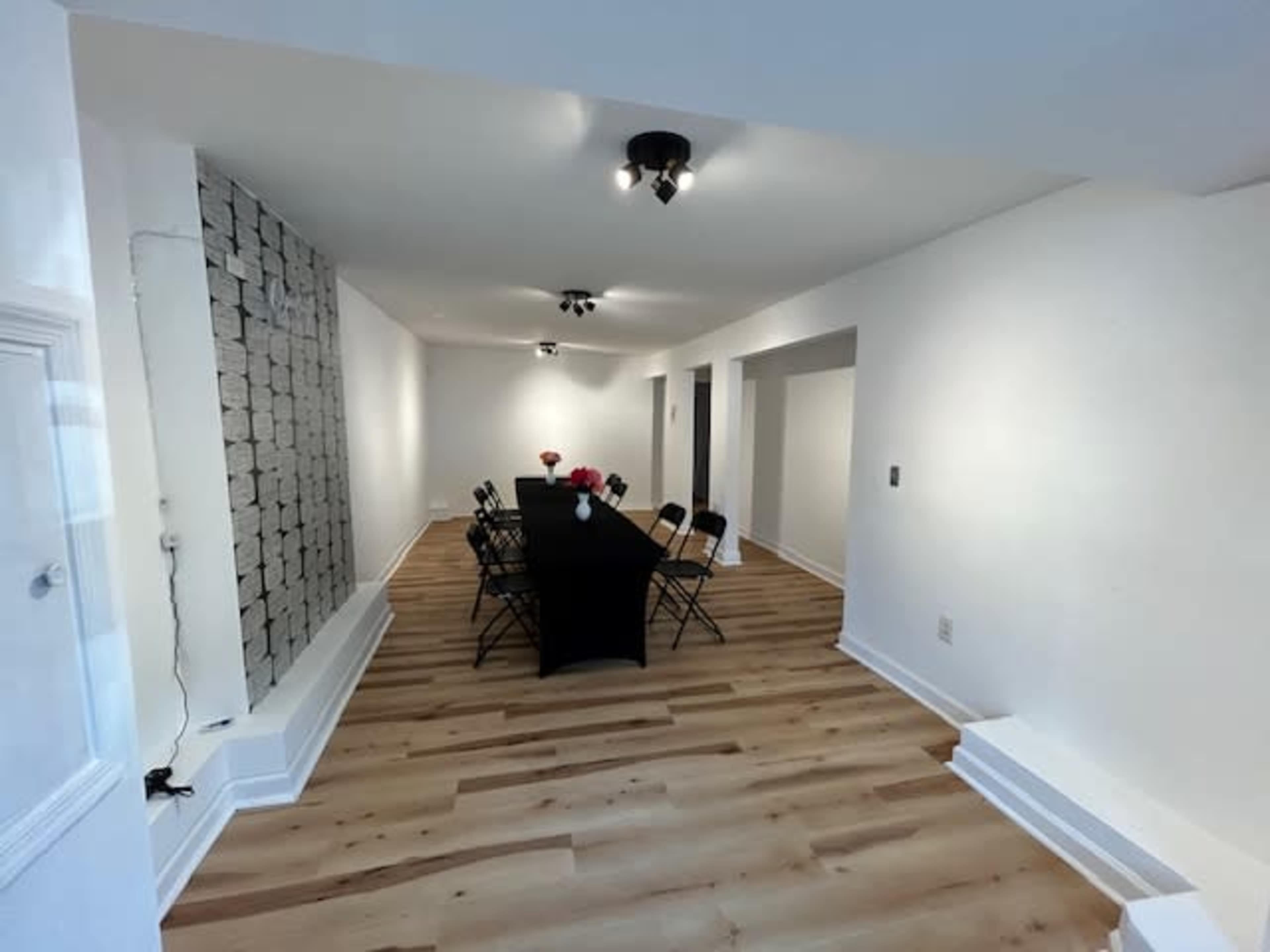 The room features a long black table surrounded by chairs, with illuminated walls and a light wooden floor.