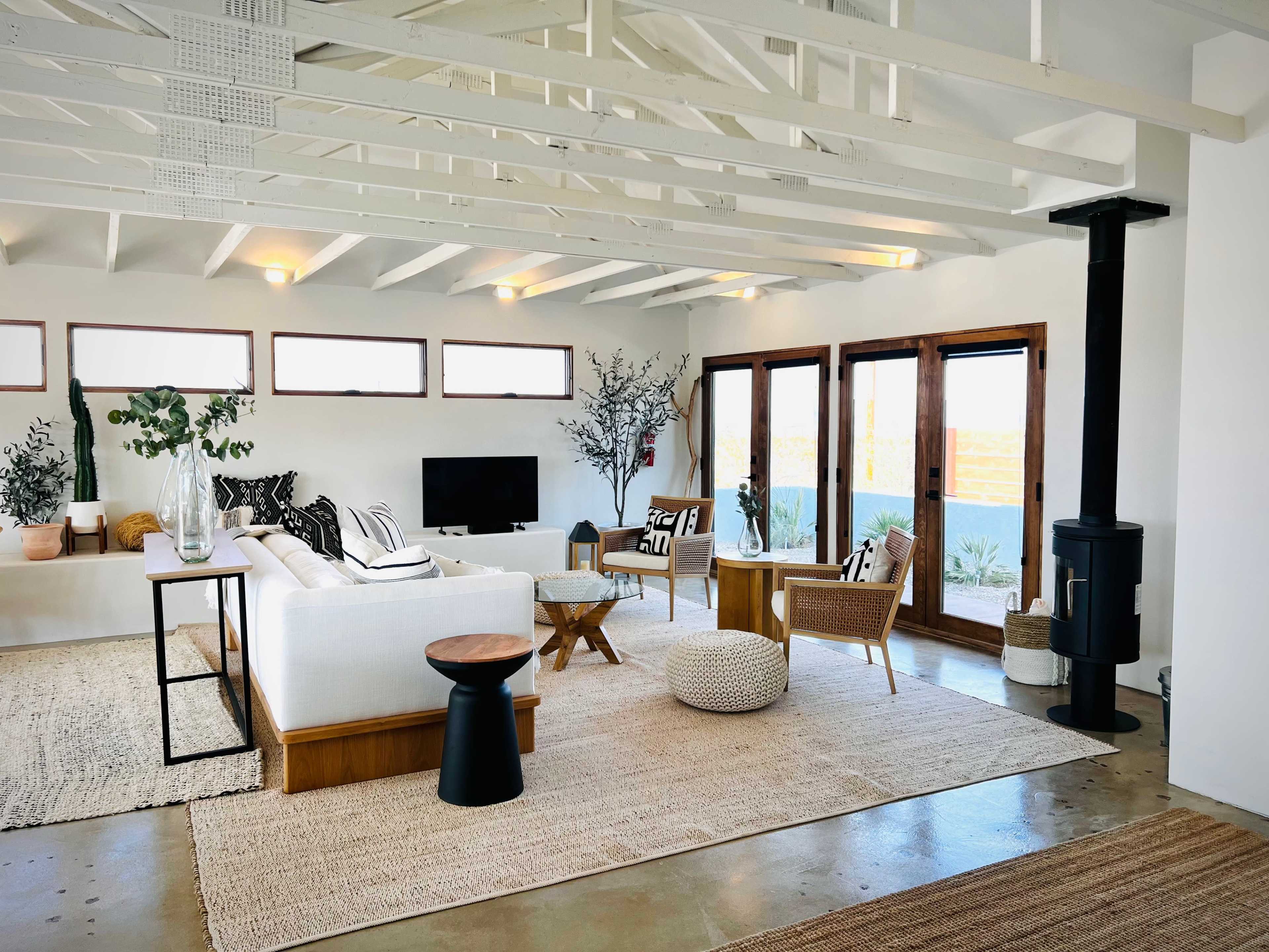 The image shows a modern living room with a white sofa, wooden furniture, and large windows allowing natural light.
