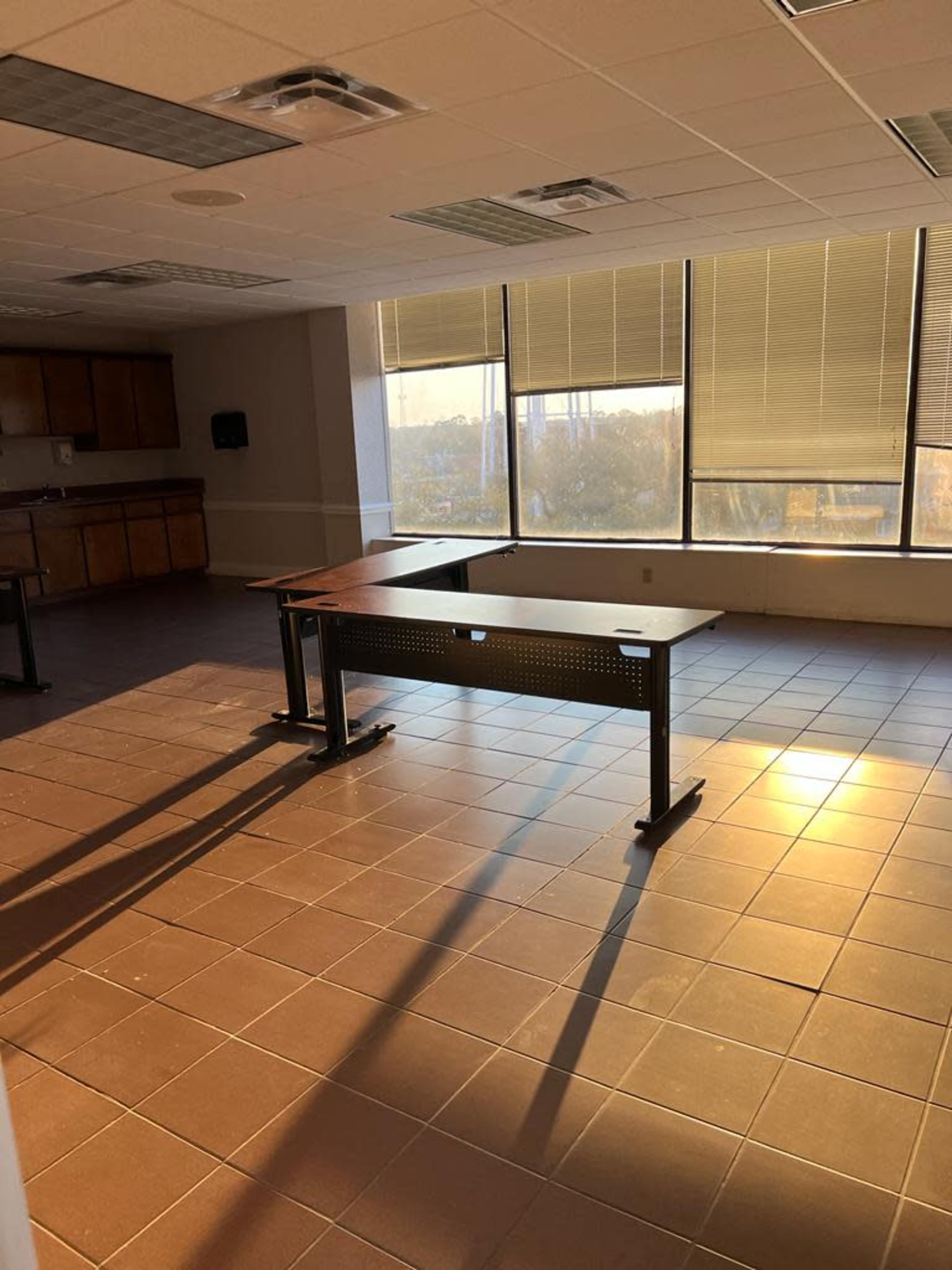 A spacious room with tile flooring features a central table and large windows allowing natural light to illuminate the space.