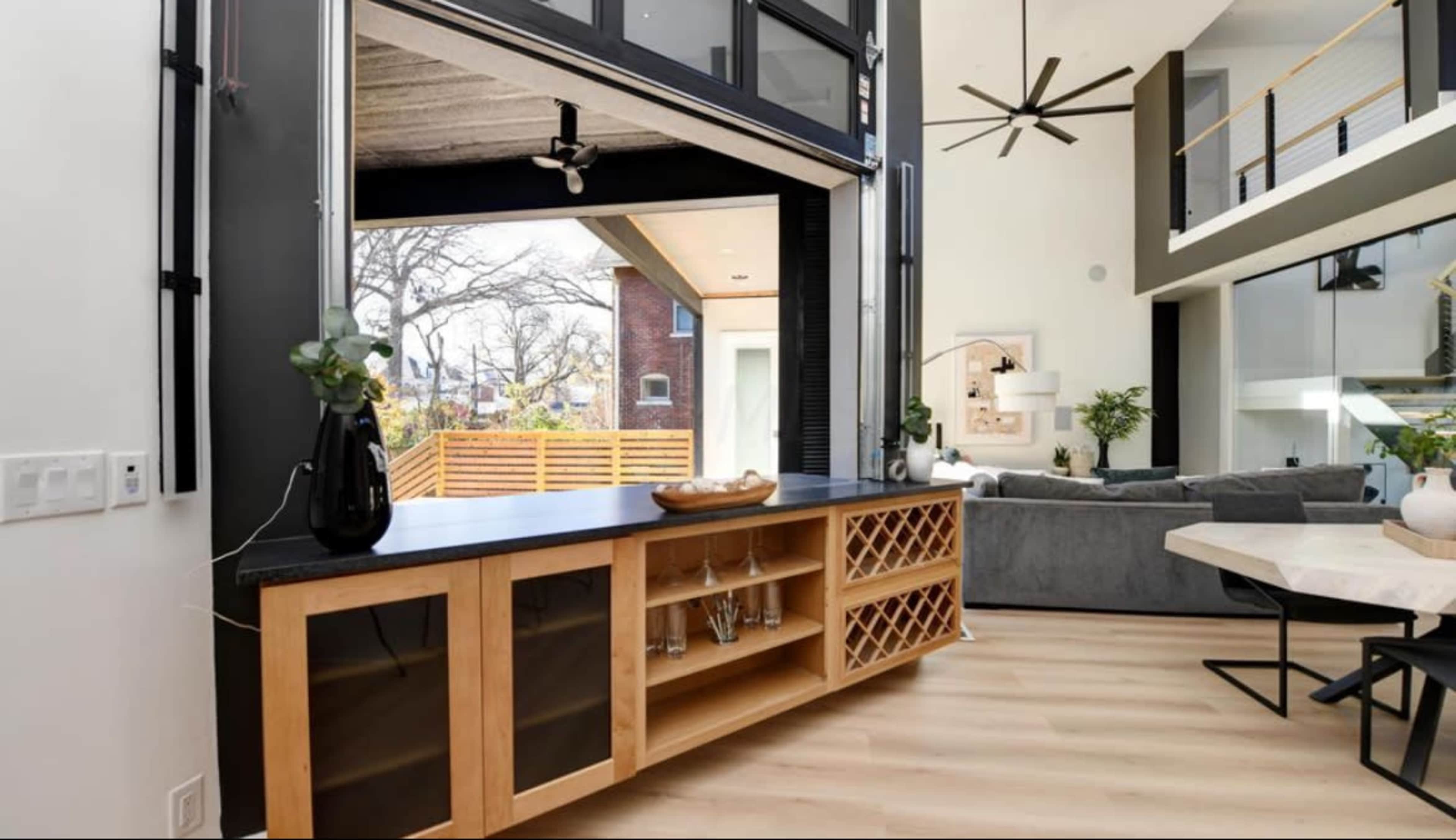 A modern living space with large glass doors opening to an outdoor area, featuring a wine rack and a countertop between the indoor and outdoor spaces.