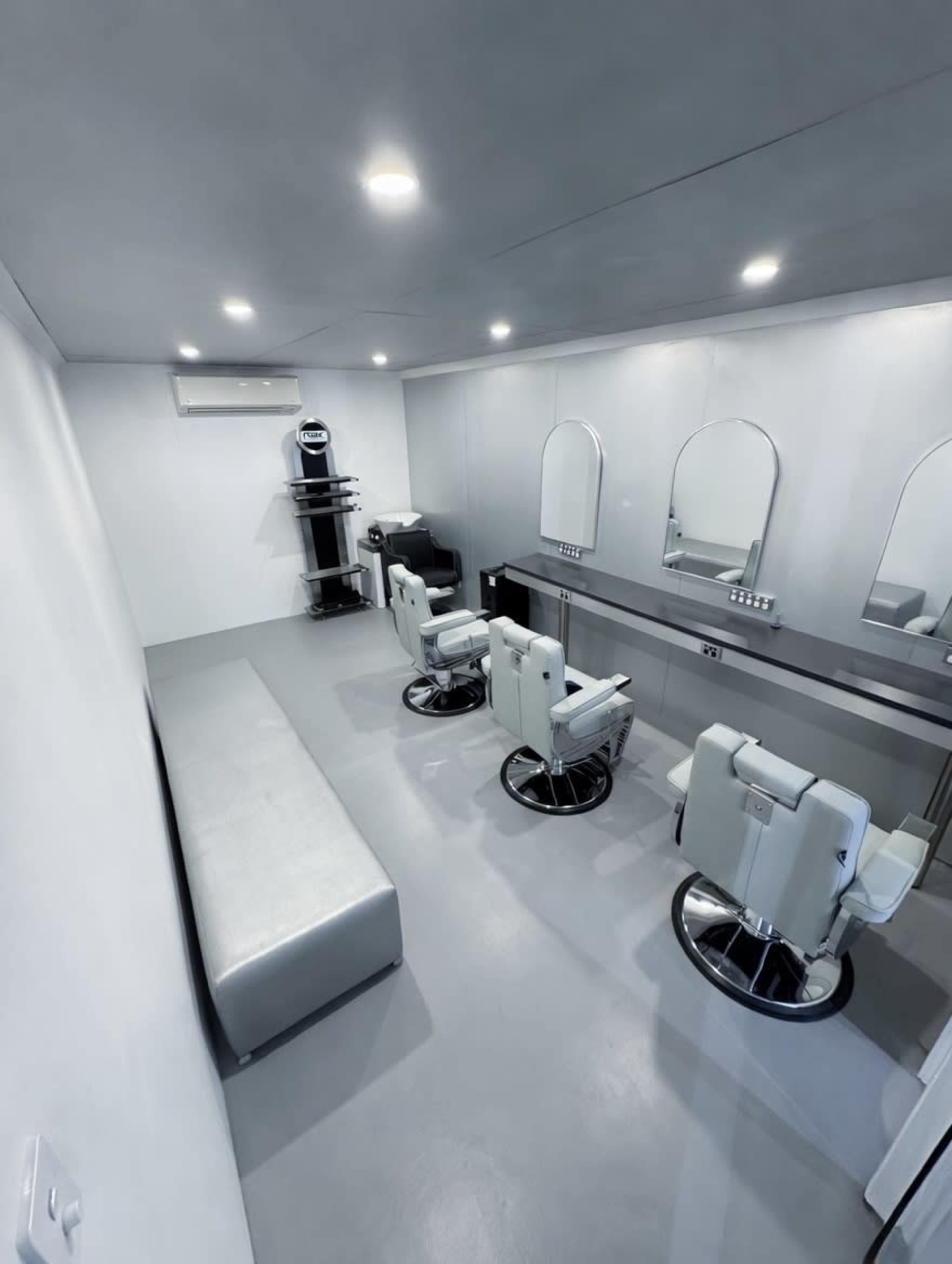 The image shows a modern hair salon interior with three styling chairs, mirrors, and a seating area.