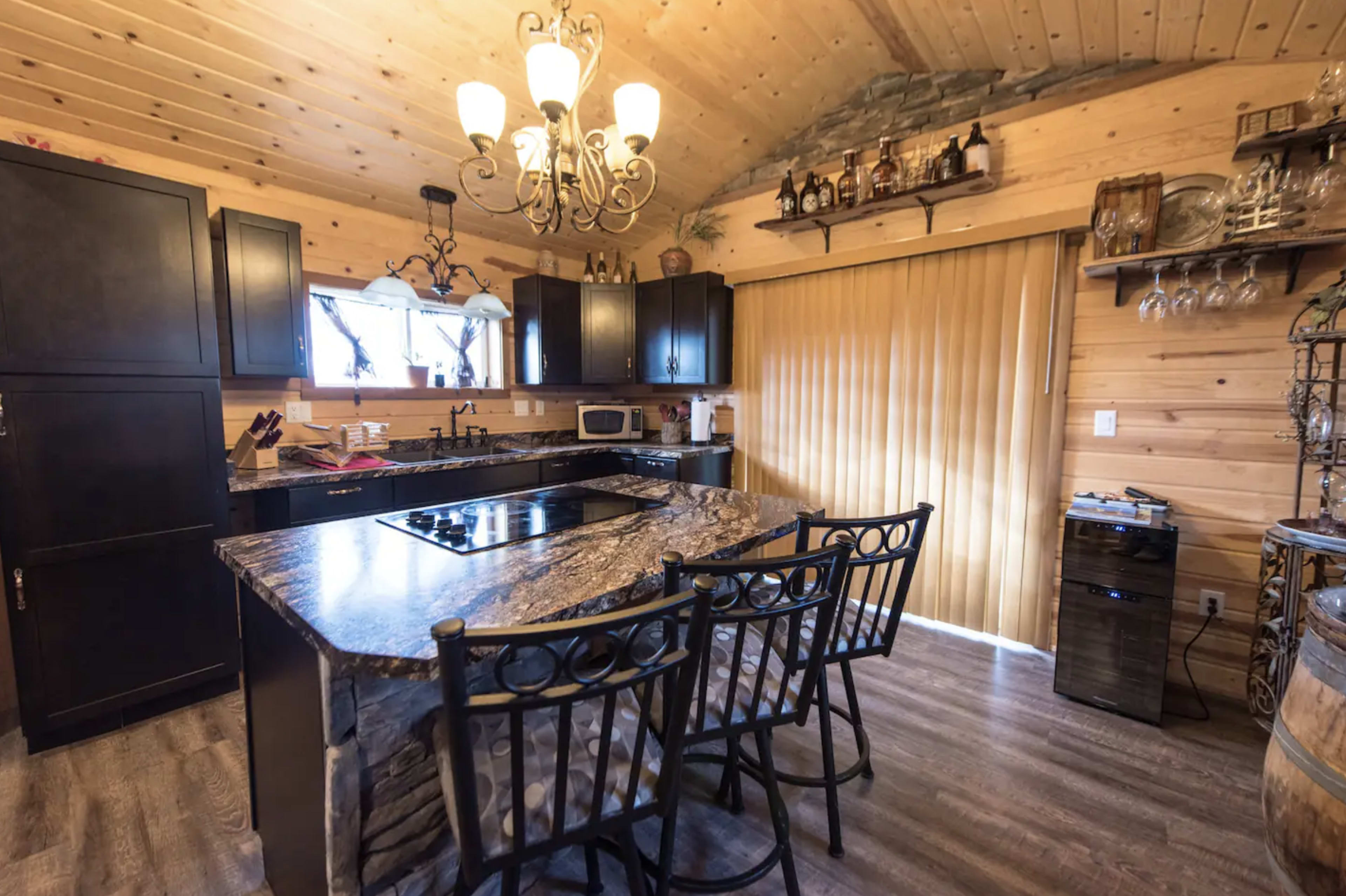 A wooden kitchen features a dark cabinetry setup, a large island with seating, and a chandelier overhead.