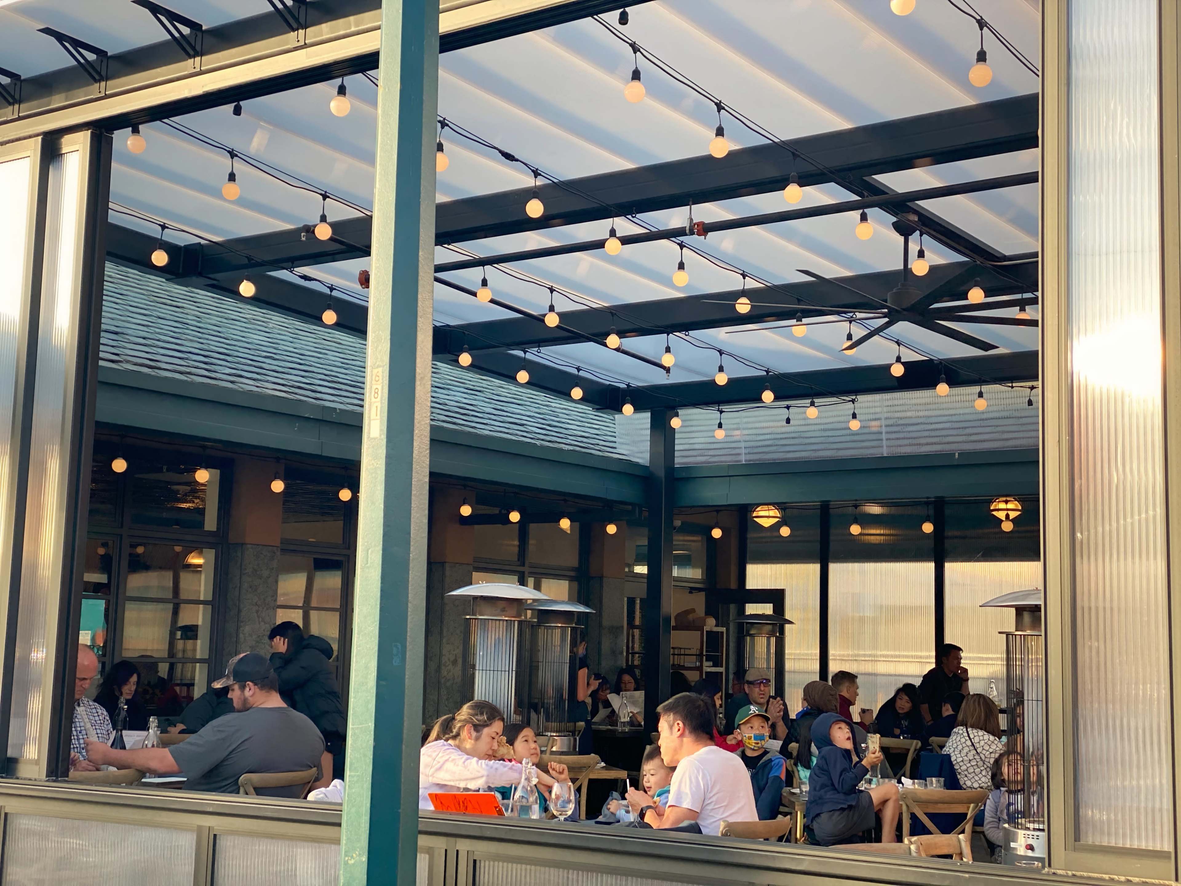 A bustling indoor dining area with people seated at various tables, illuminated by string lights overhead.