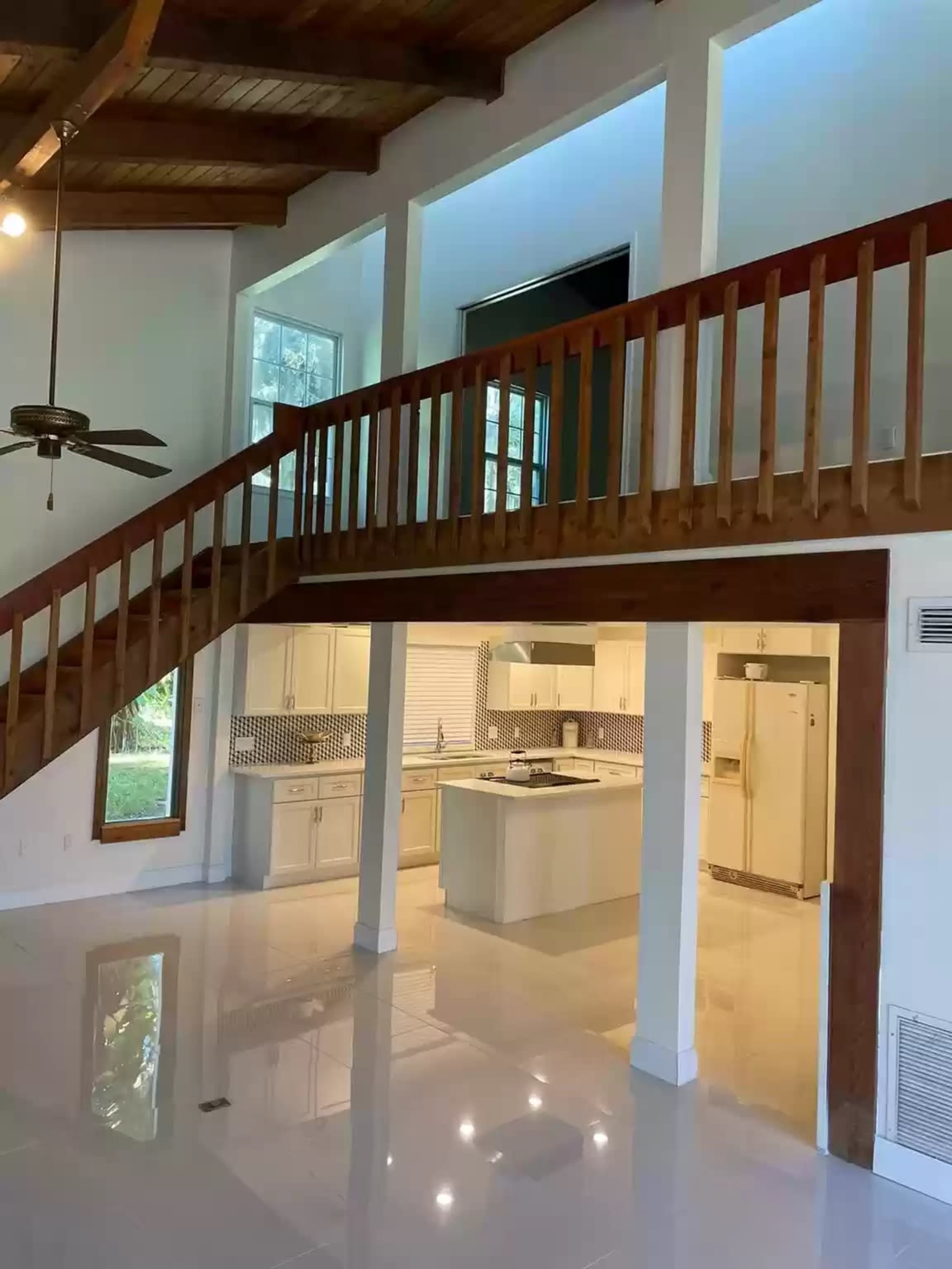 A spacious living area featuring a wooden staircase and a modern kitchen with white cabinetry and glossy floors.