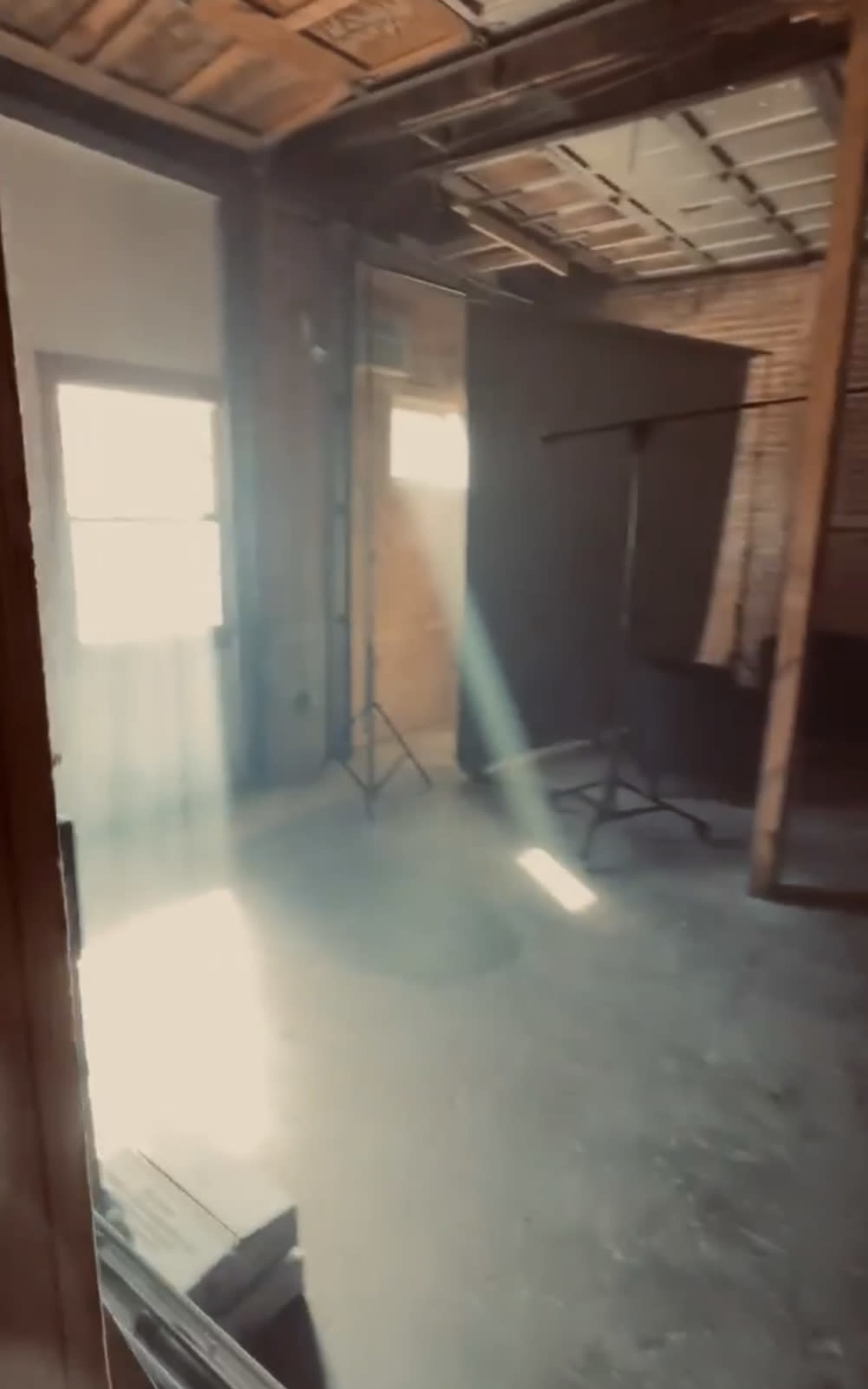 An empty room with wooden walls and beams, featuring a beam of light streaming through a window and casting a shadow on the floor.