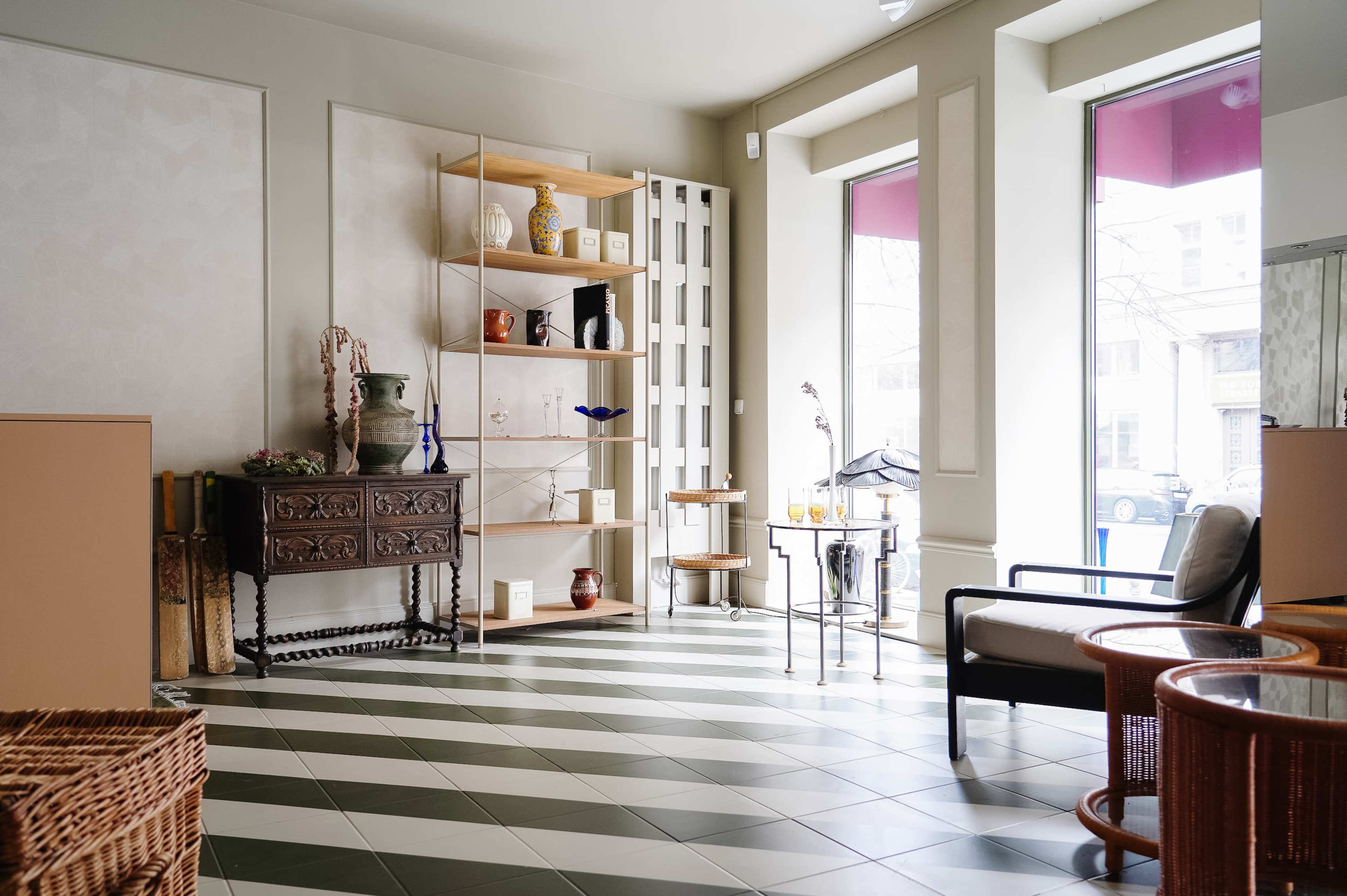 The interior features a neatly arranged space with green and white patterned tiles, a wooden shelf with decorative items, and seating areas by large windows.