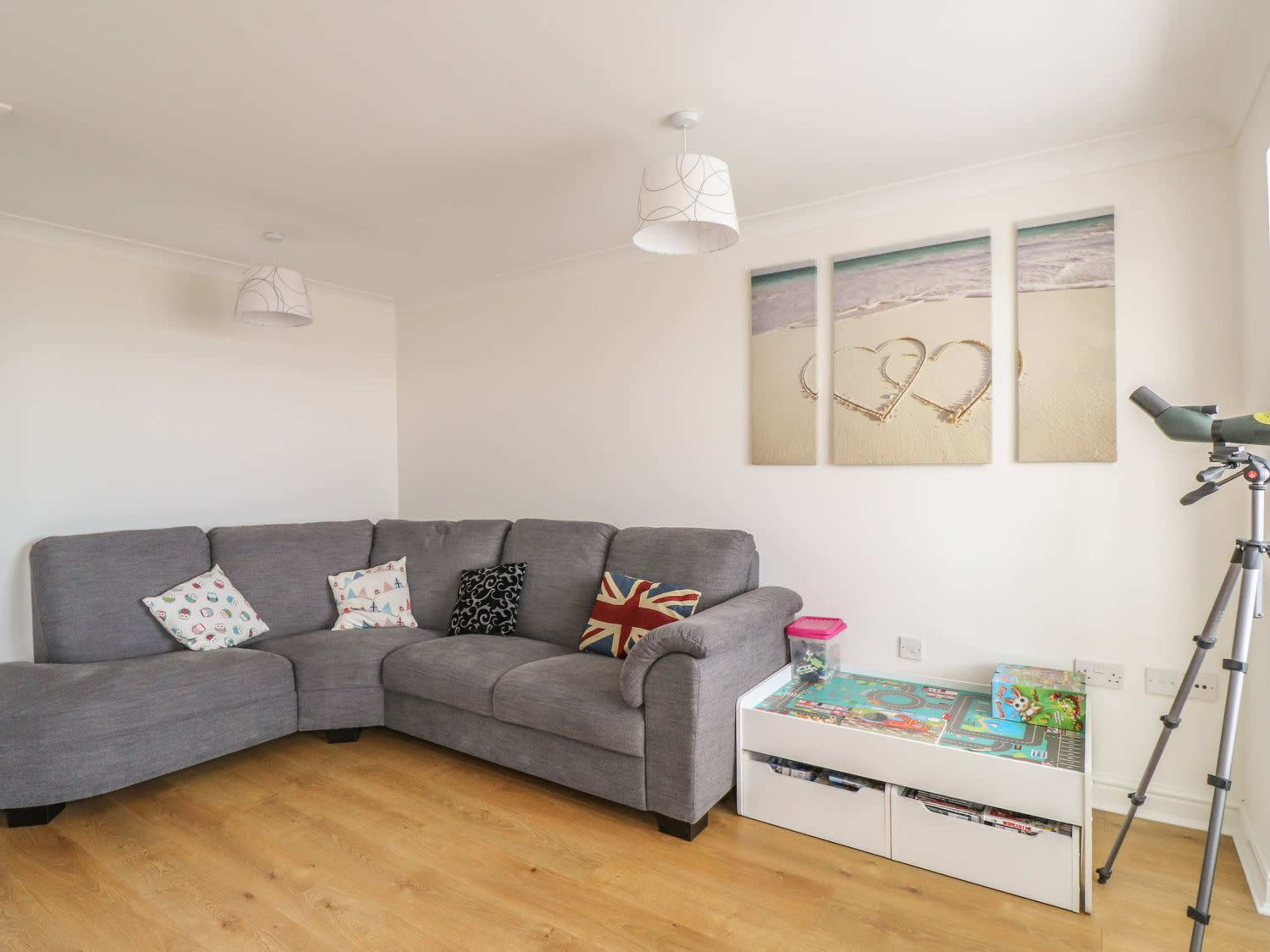 A gray sectional sofa with decorative cushions is positioned in a light-colored room alongside a white storage unit filled with toys and a telescope.