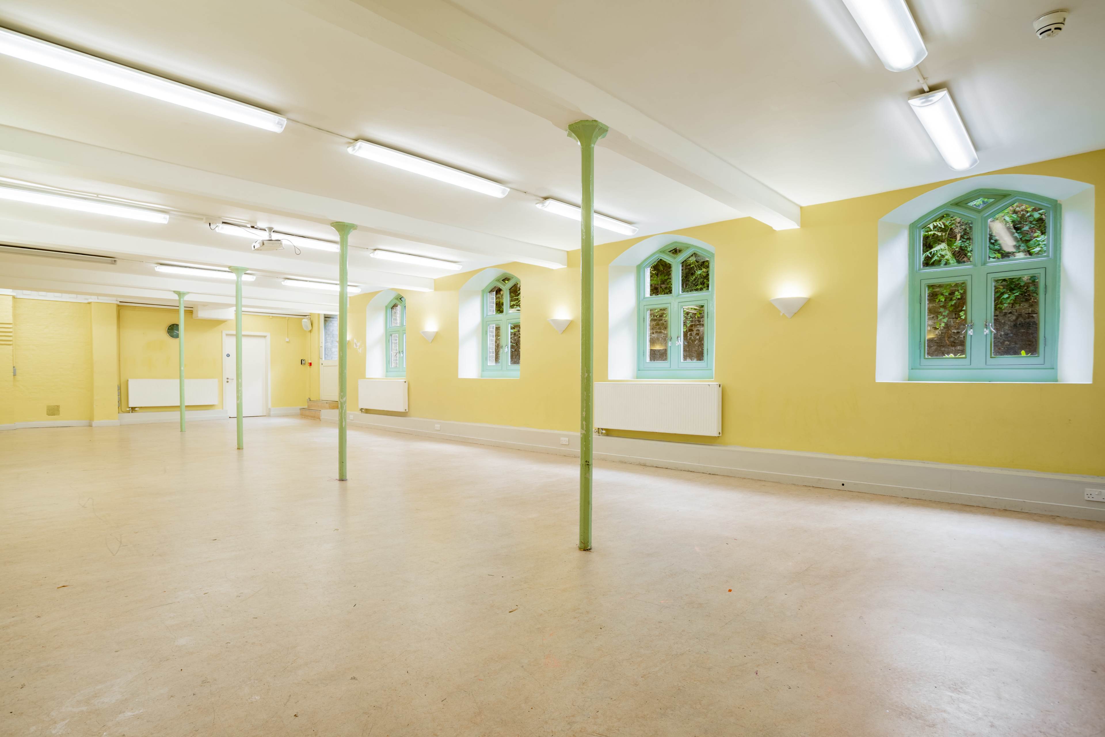 A spacious interior room with yellow walls, arched windows, and green columns.