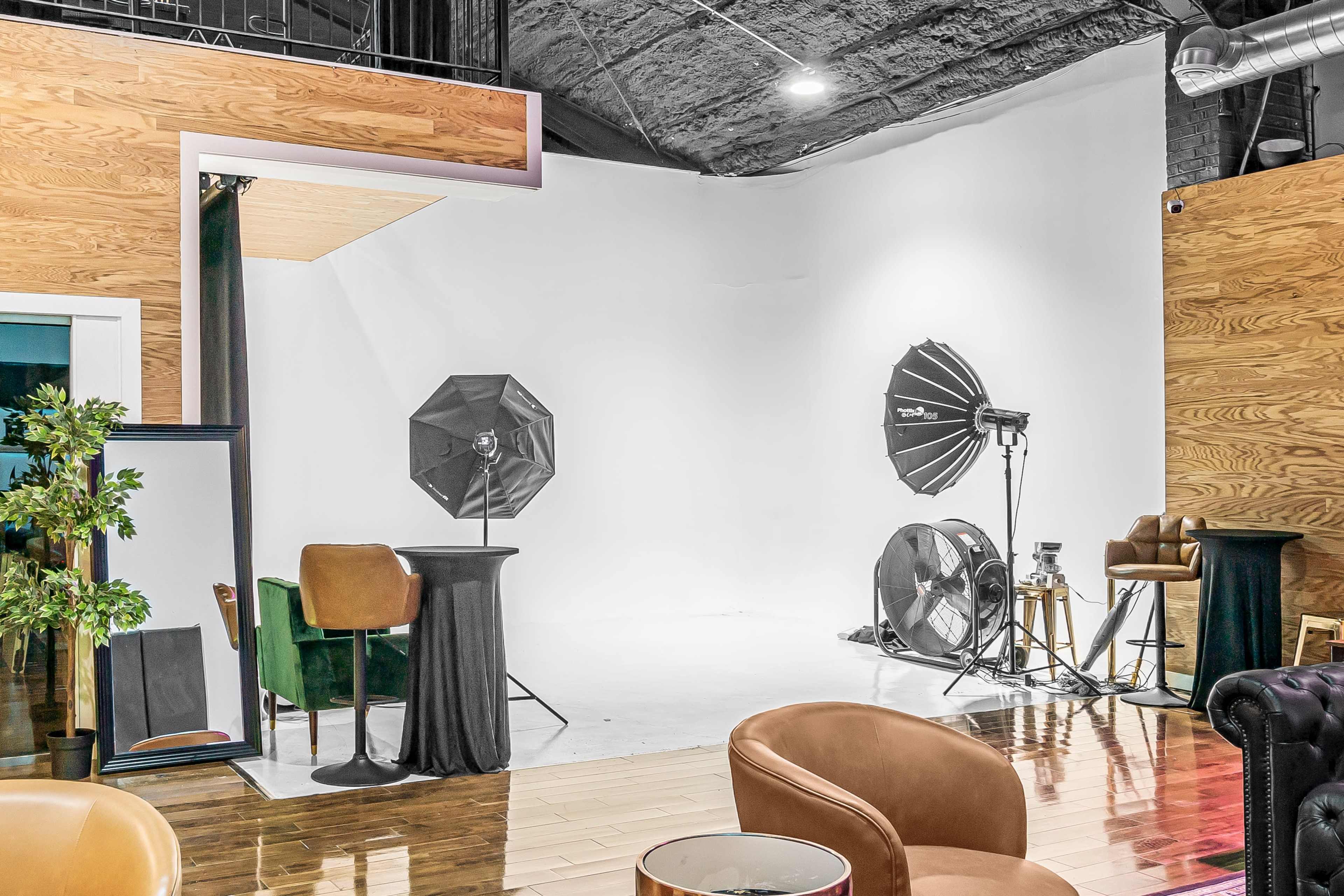 The image shows a photography studio with a white backdrop, lighting equipment, and various furniture pieces.