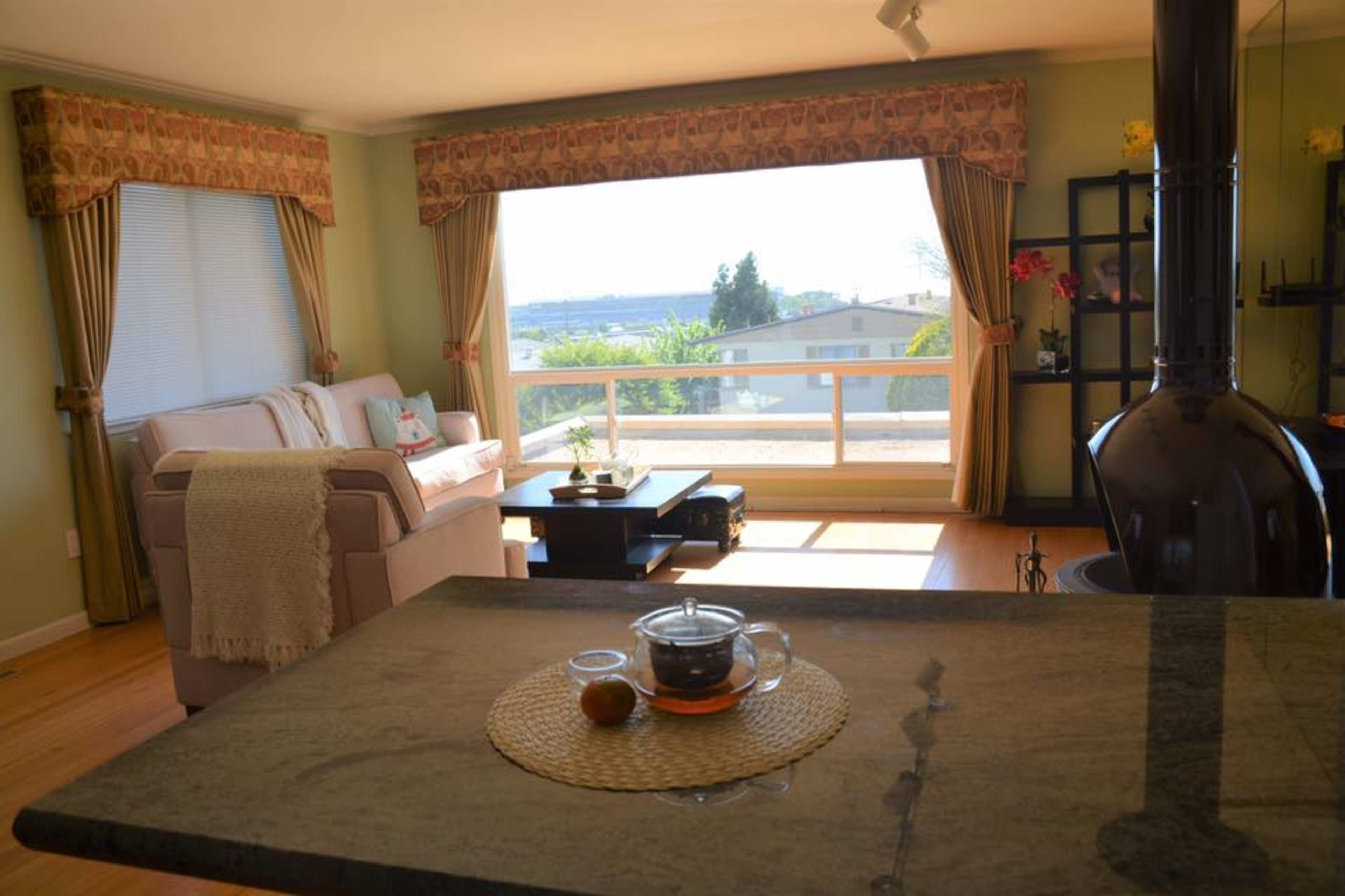 A bright living room features a beige sofa, a coffee table, and a large window overlooking a scenic view.