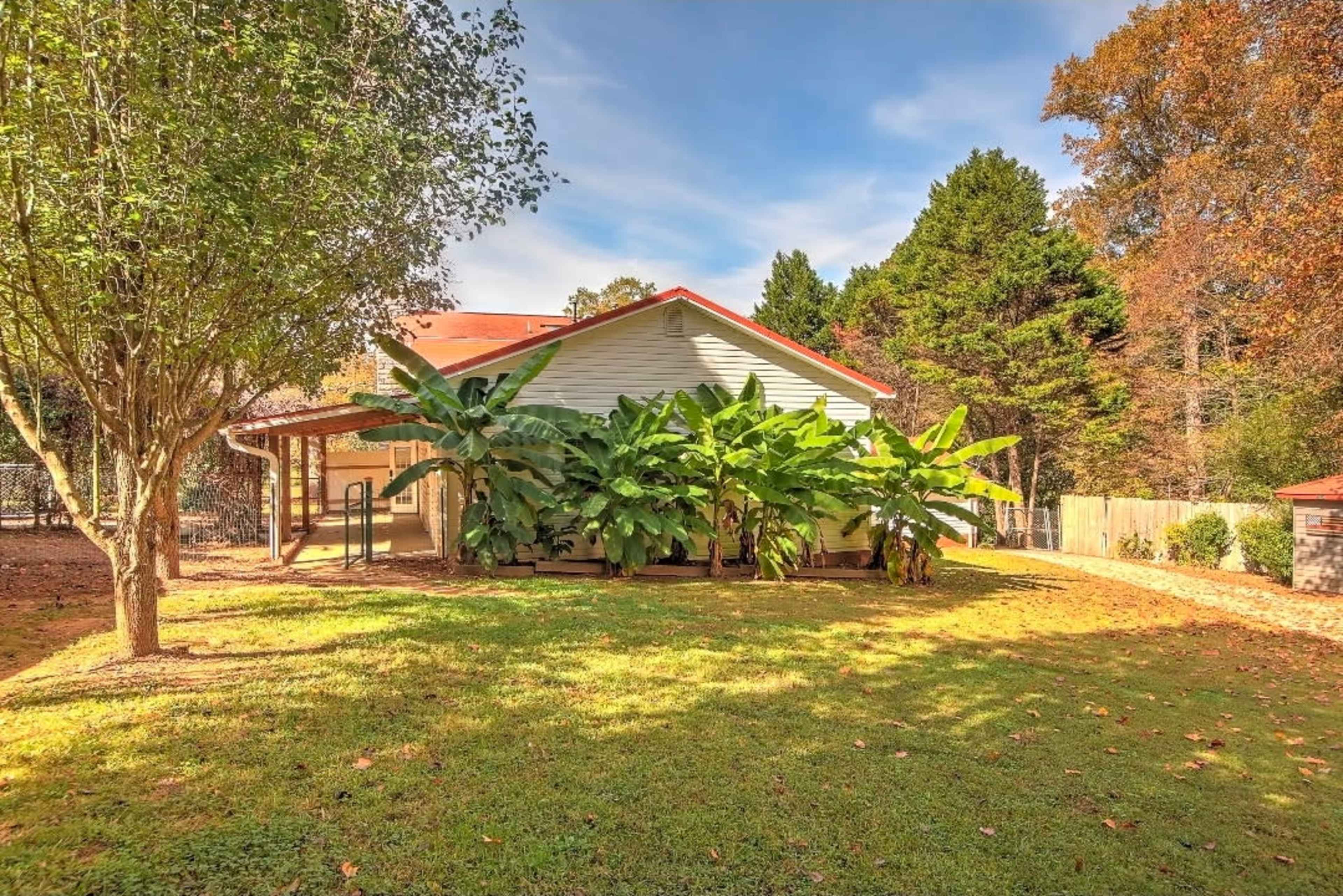The image shows a single-story house with a red roof, surrounded by large banana plants and trees in a grassy yard.
