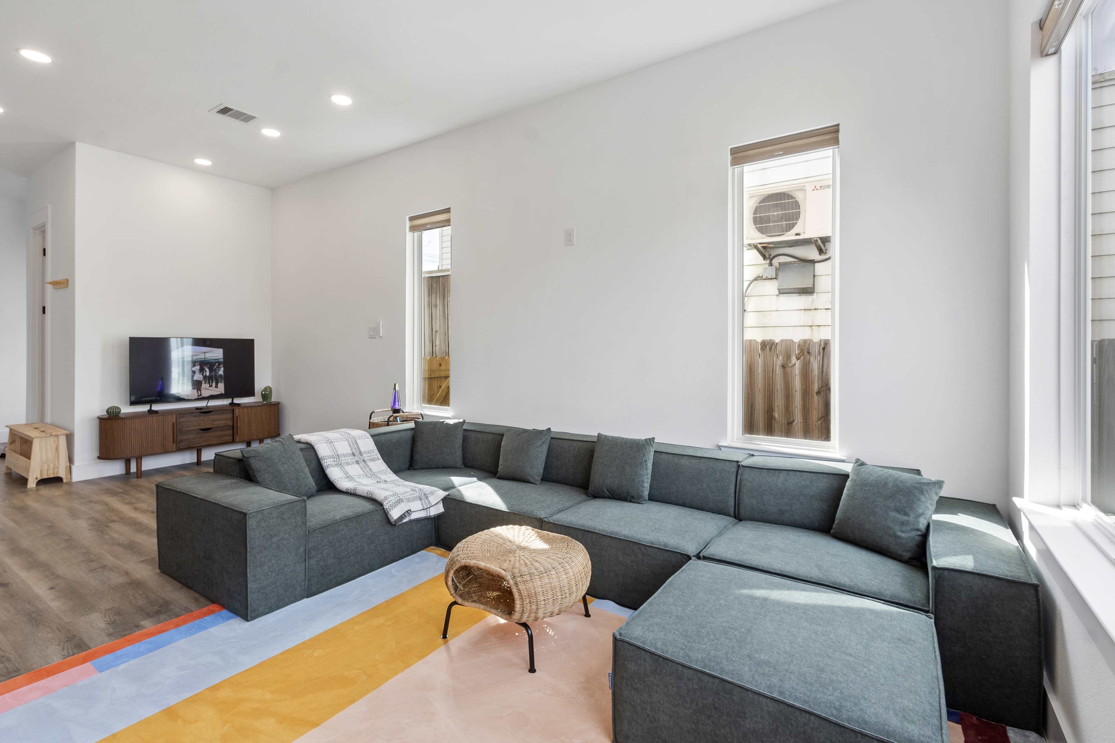 The image shows a modern living room featuring a large sectional sofa, a small round coffee table, and a television on a stand.