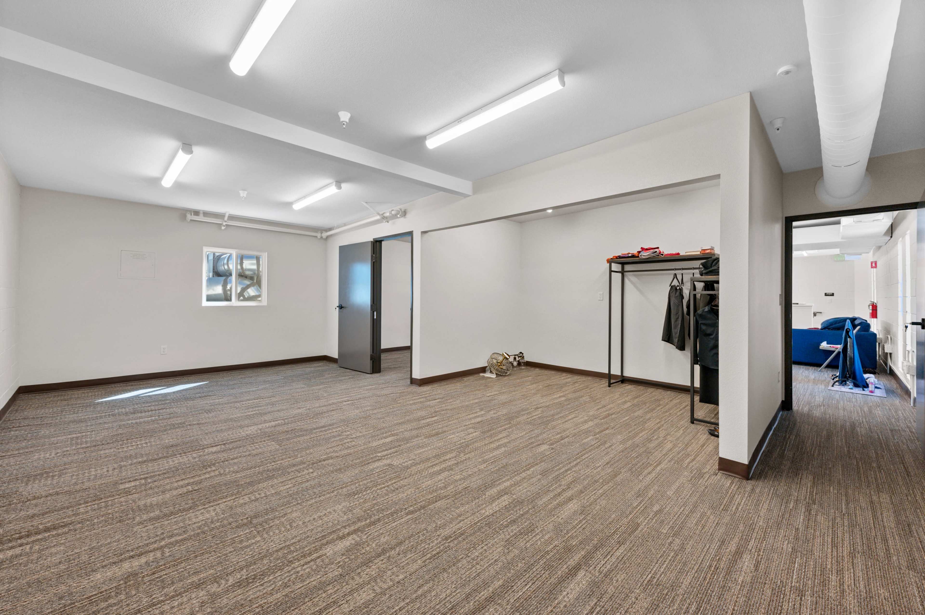 The image shows an empty room with beige walls, a light brown carpet, and a clothing rack against one wall.