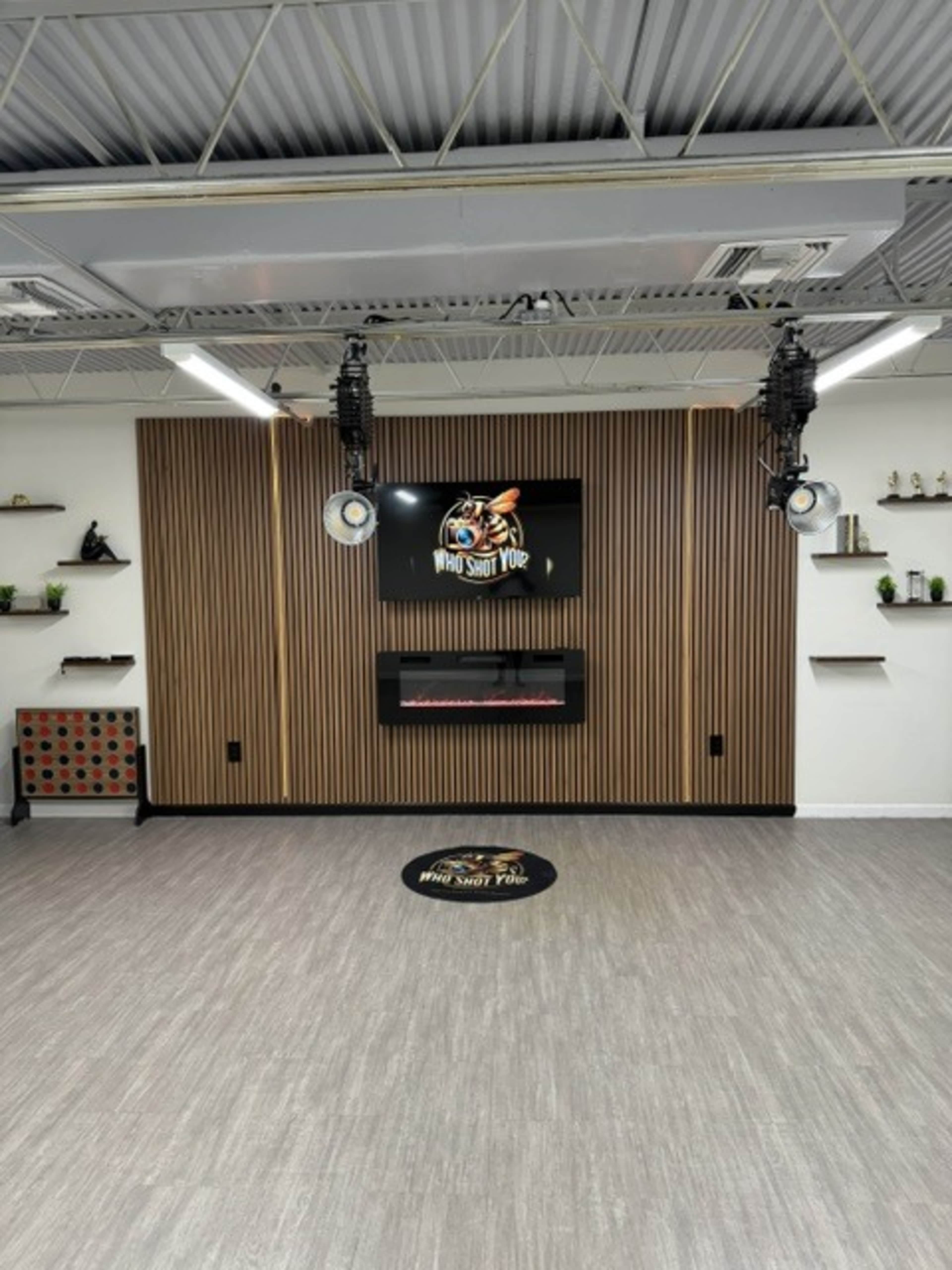 The image shows a neatly arranged interior space featuring a wooden accent wall with a television mounted above an electric fireplace and decorative shelves.